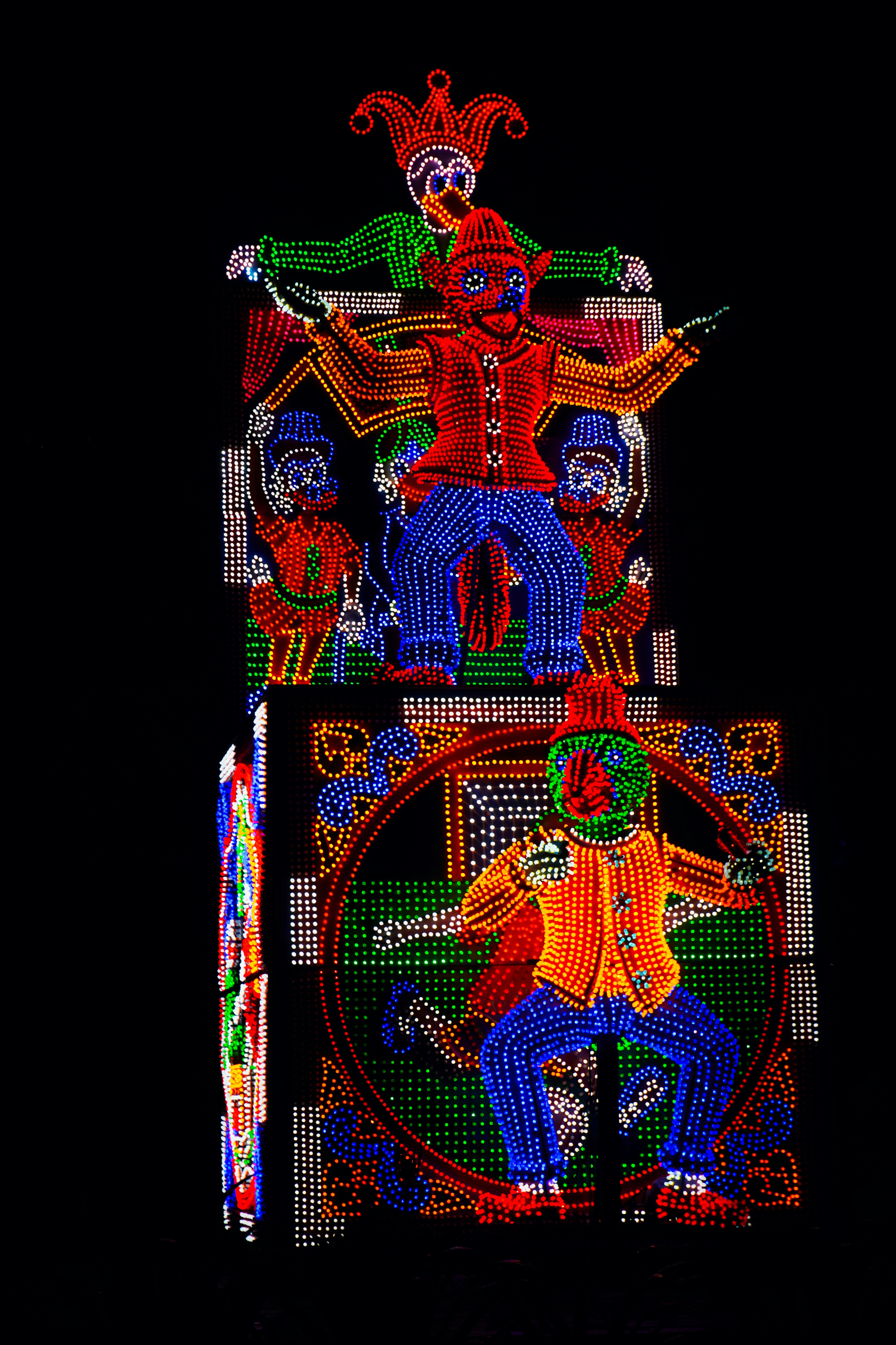 Brightly lit figures of clowns and jesters at night.