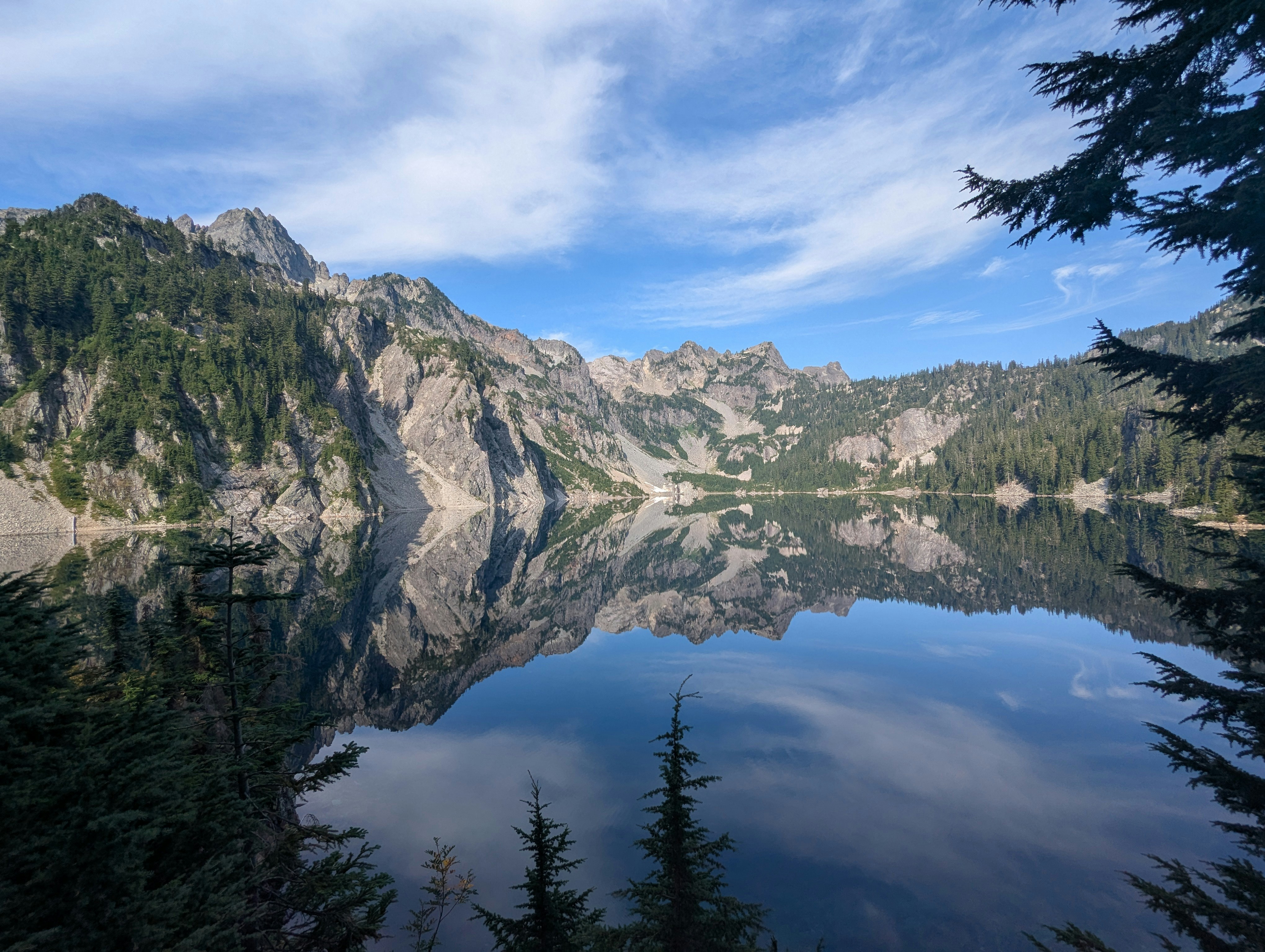 Calm lake reflecting mountains and trees under blue sky.