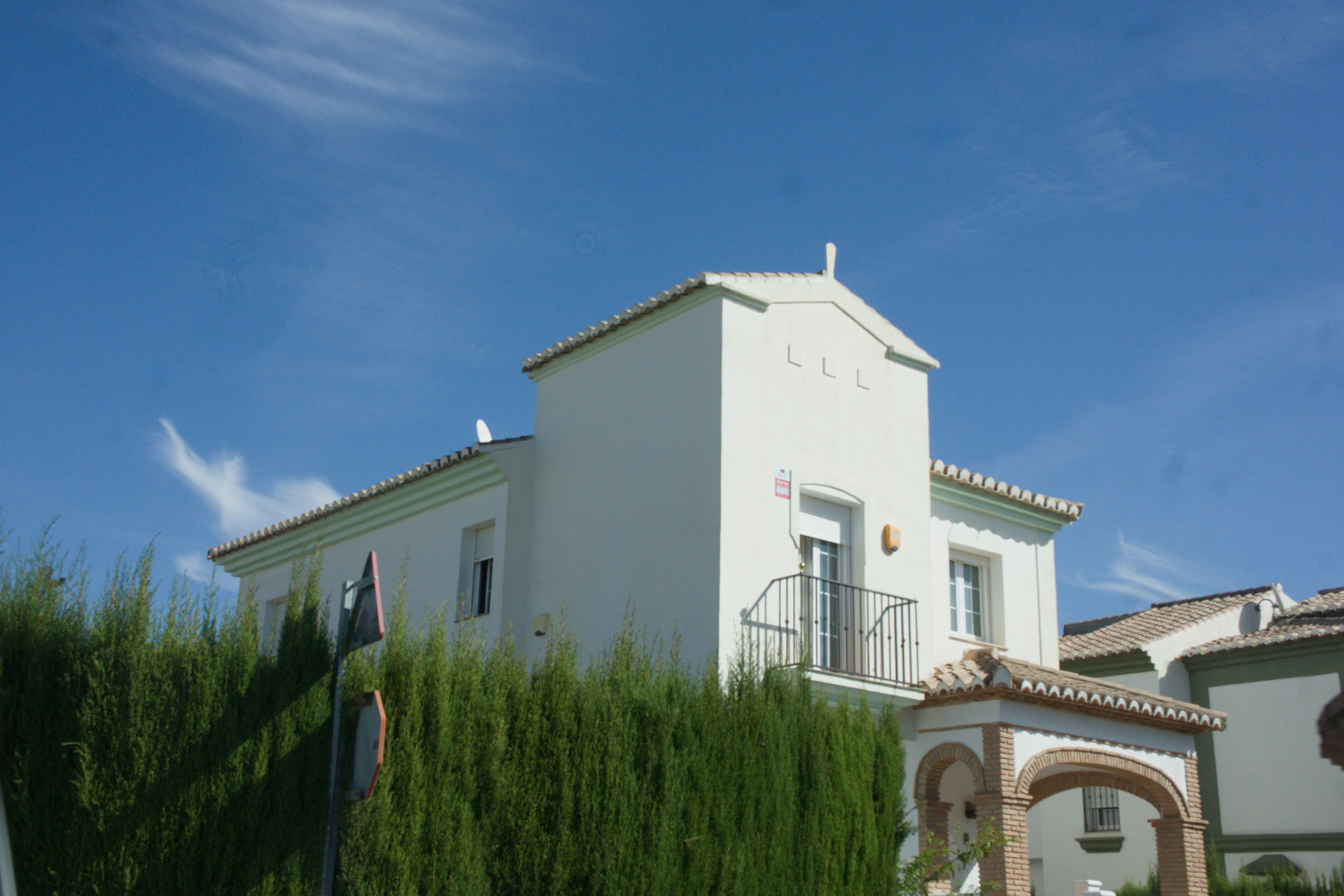 White modern house behind green hedge under blue sky