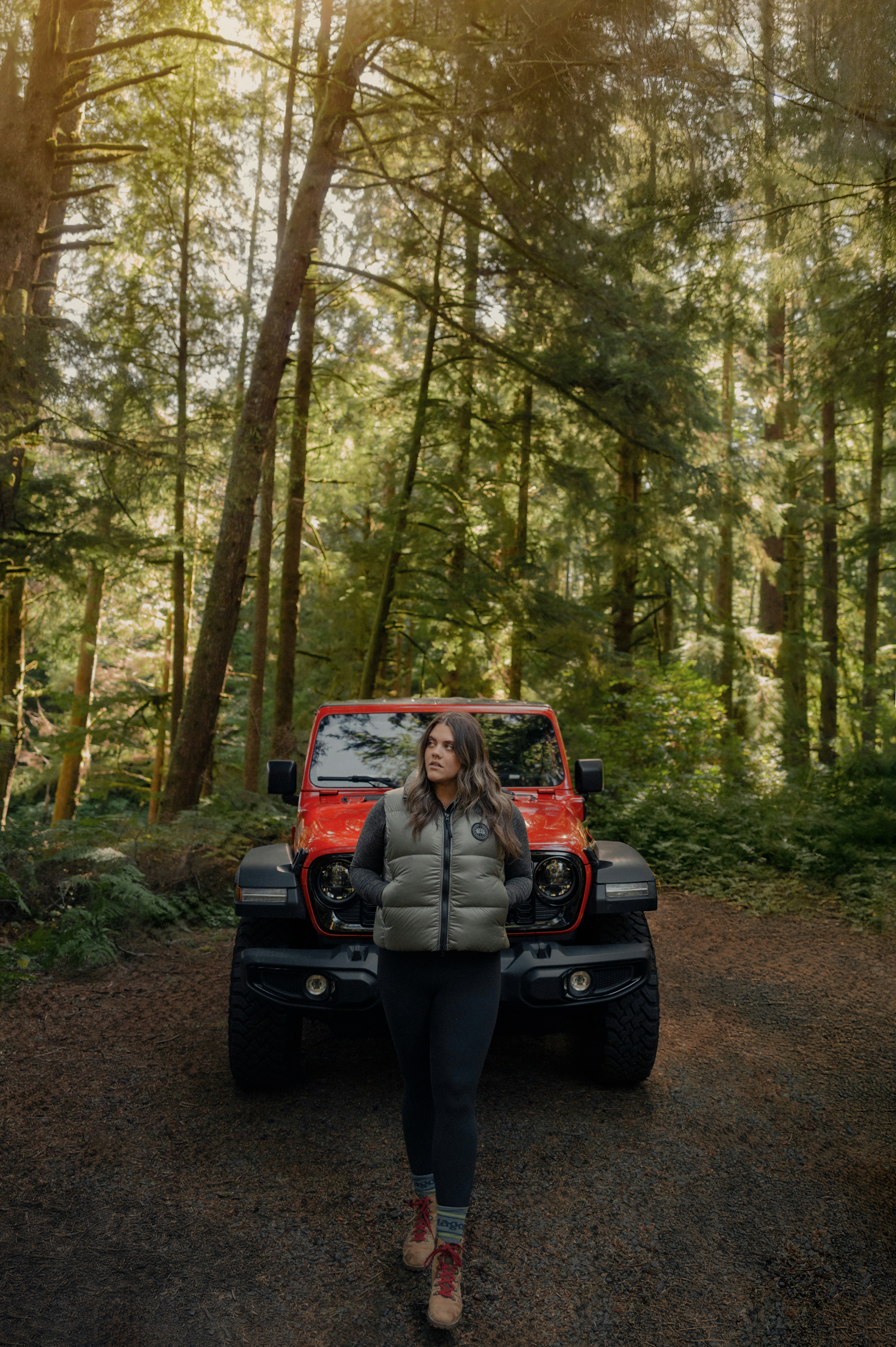 Woman standing in front of red jeep in forest