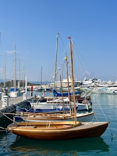 Wooden sailboat docked in a marina with yachts.