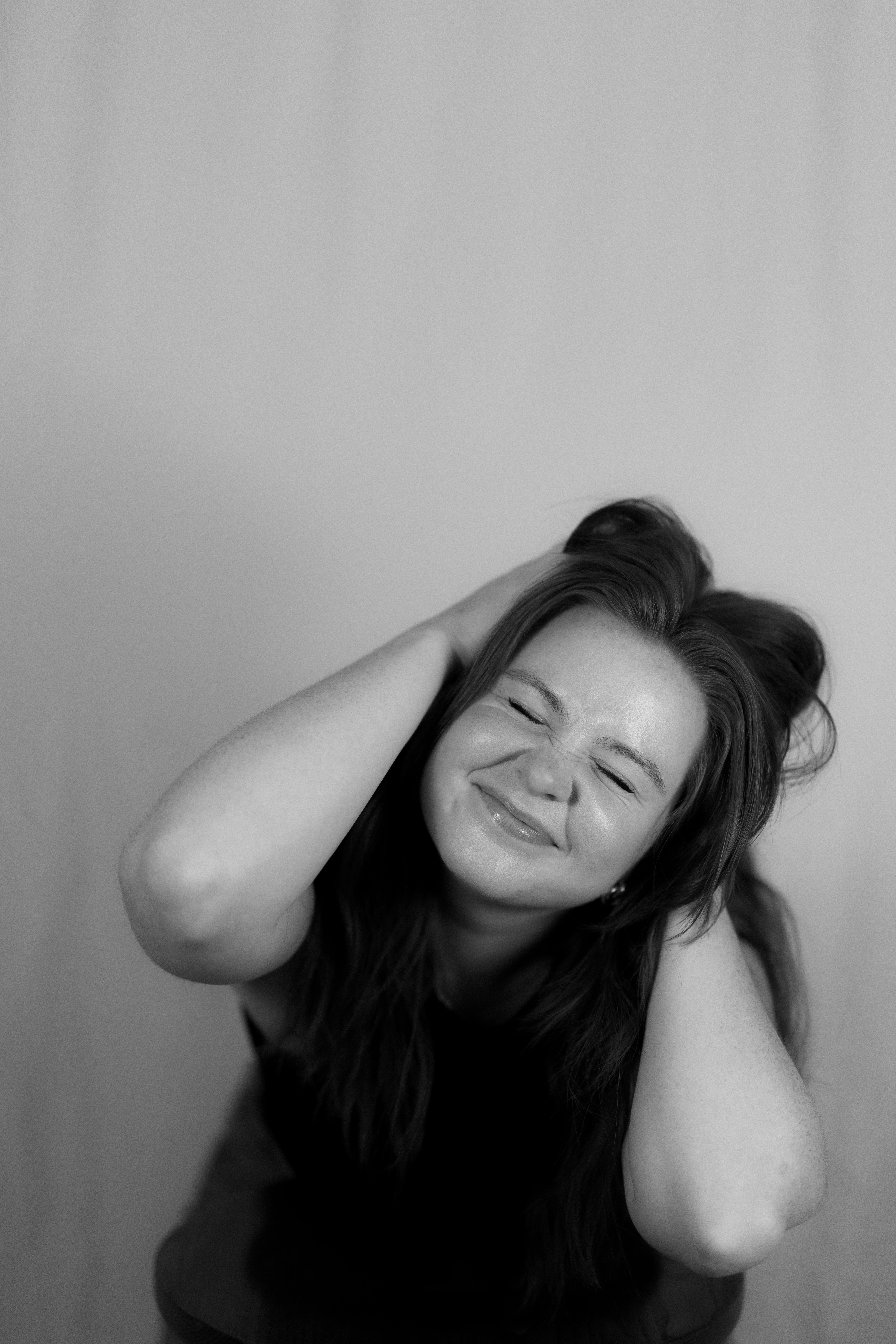 woman with eyes closed, hands in hair, smiling