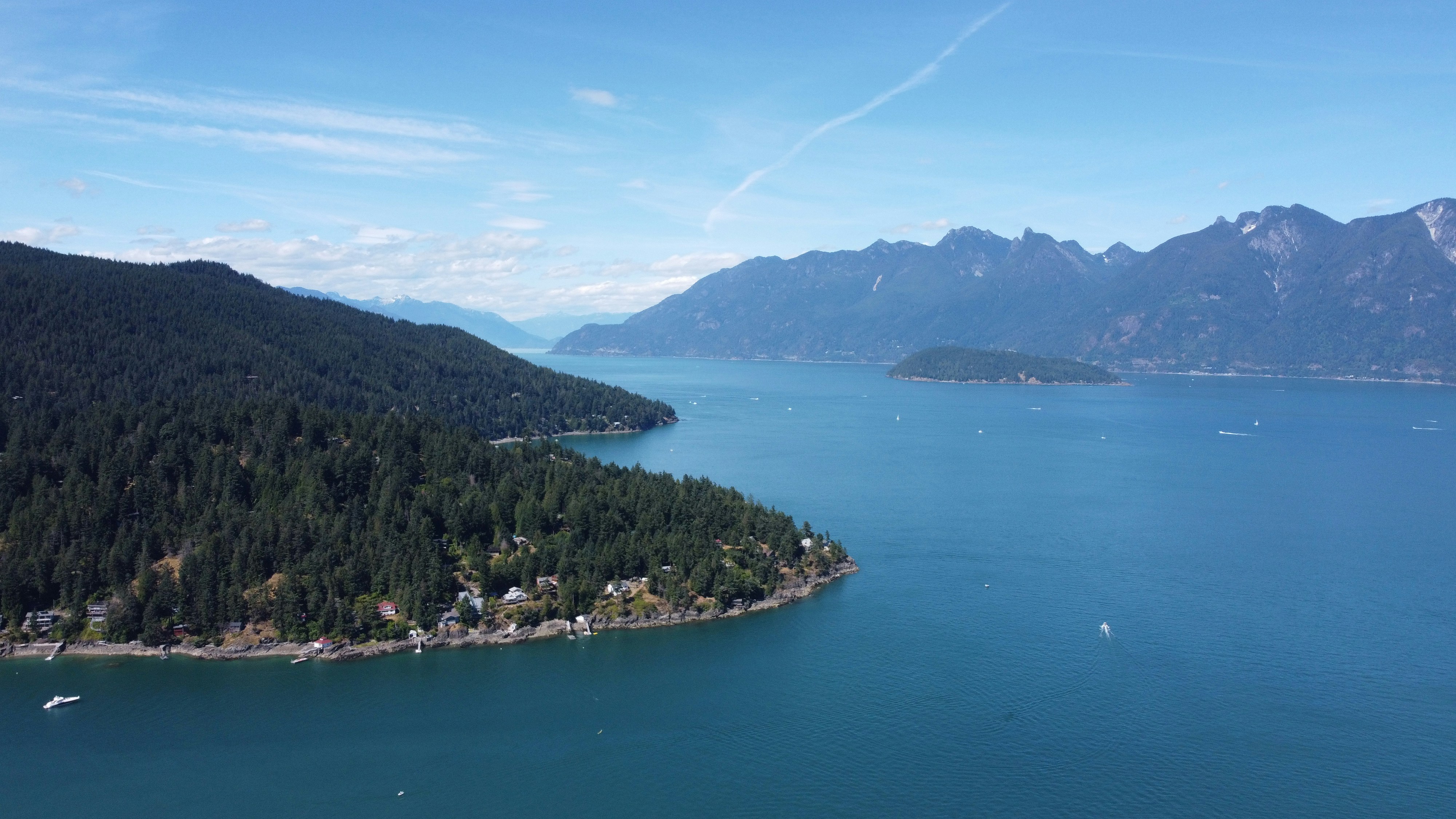 The forested shore of Bowen Island runs out into the blue water of Howe Sound below the Coast Mountains.
