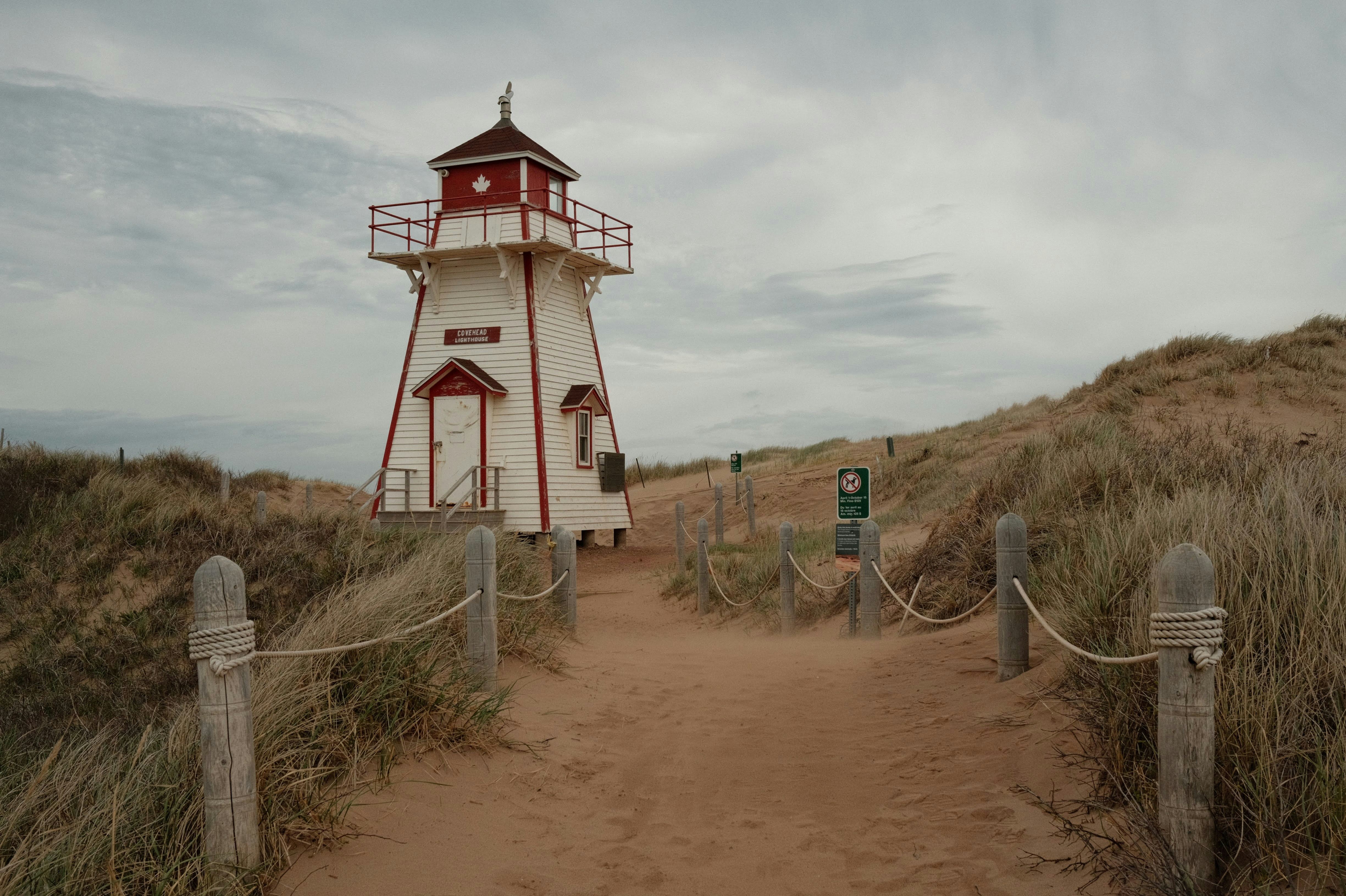 A white lighthouse stands by a sandy path.