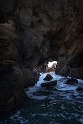 Waves crash into a dark sea cave opening.