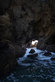 Waves crash into a dark sea cave opening.