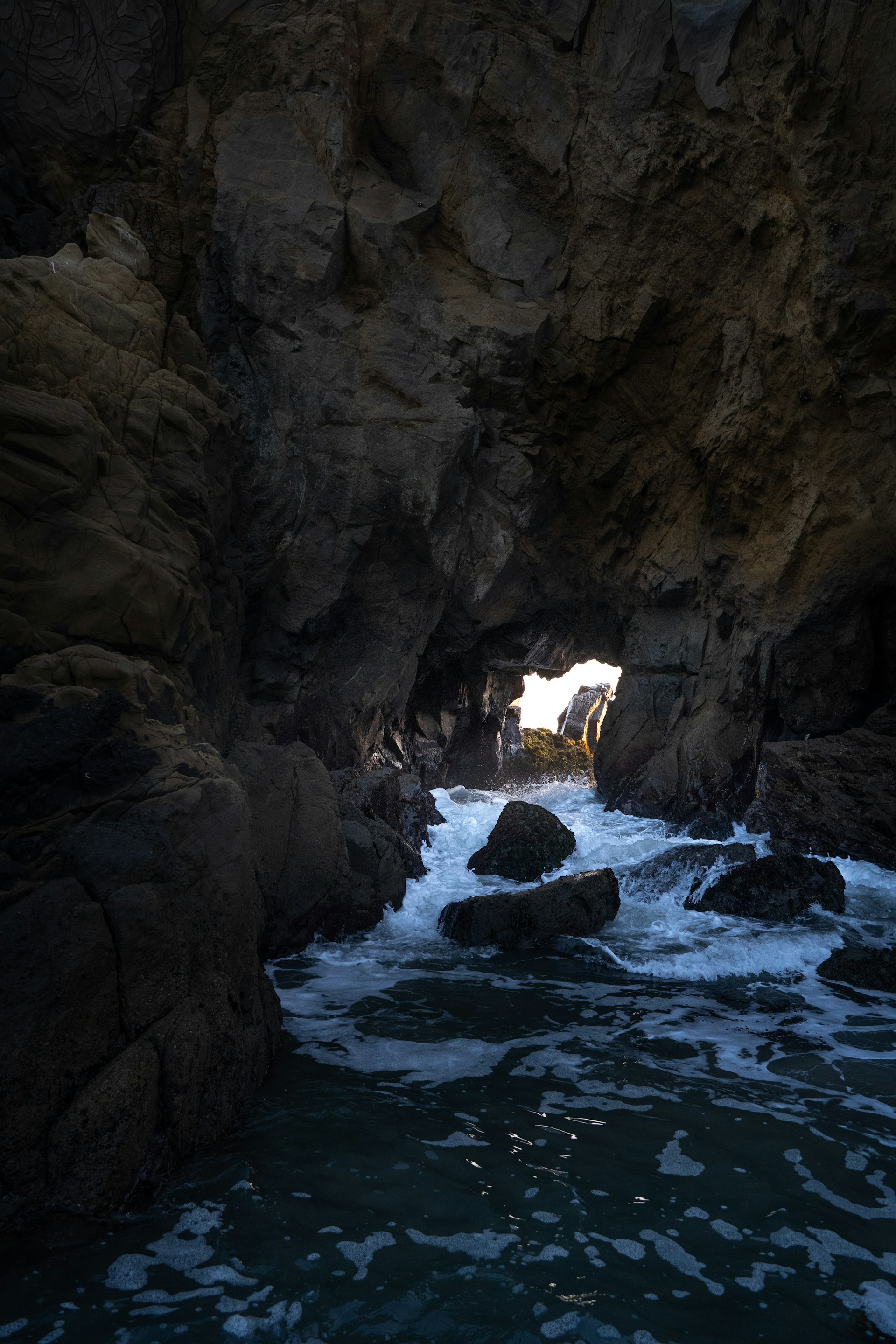 Waves crash into a dark sea cave opening.