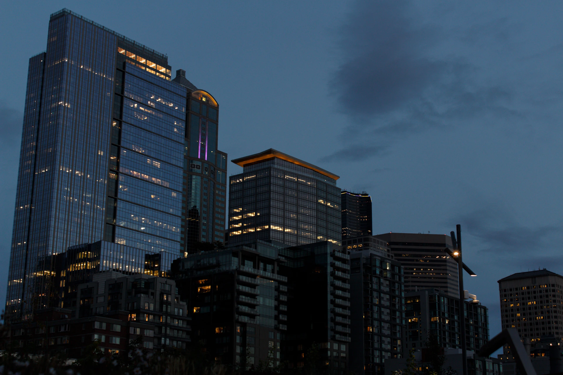 Modern skyscrapers illuminated at dusk with cloudy sky.