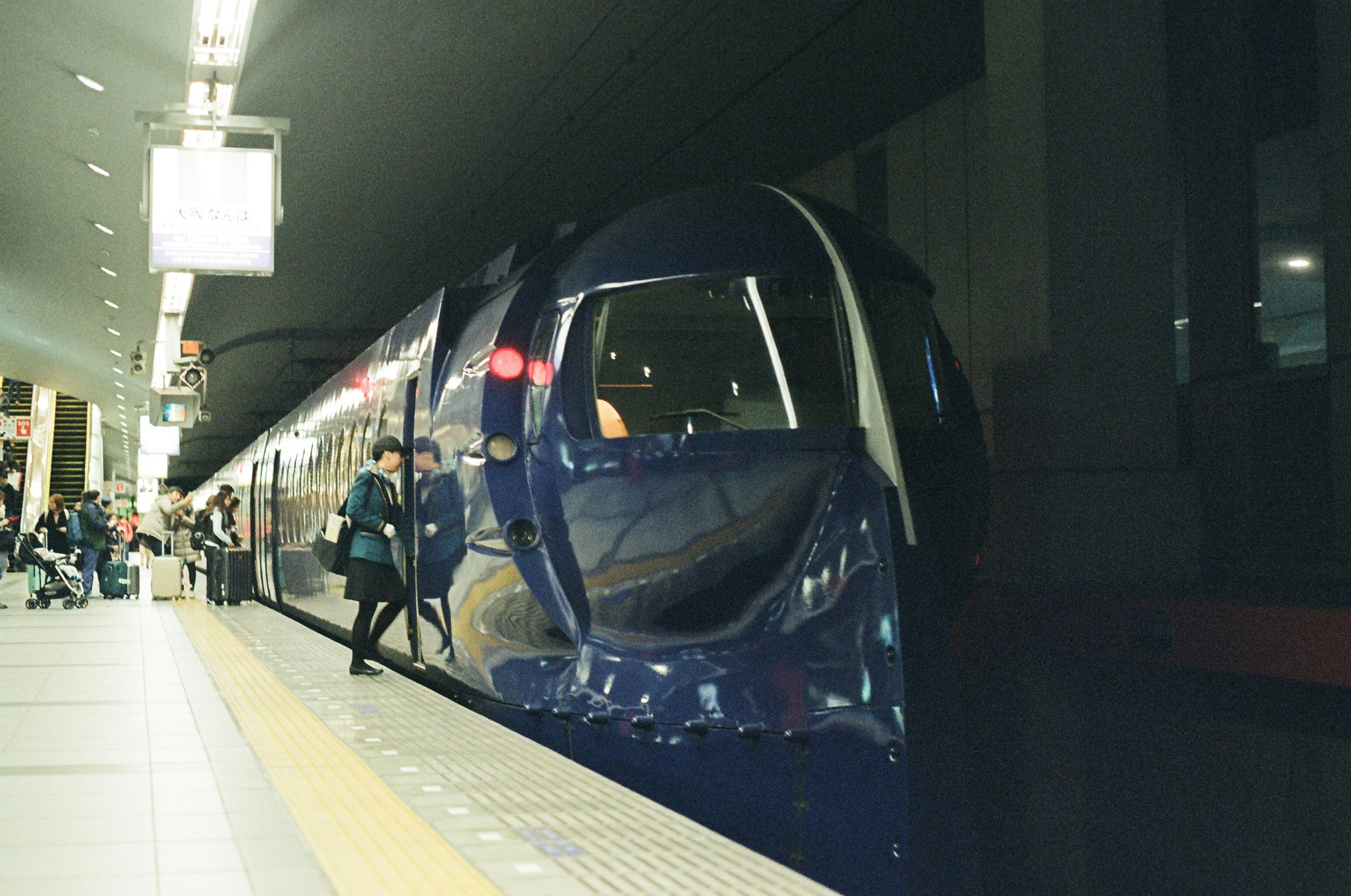 Blue train at a station platform with people.