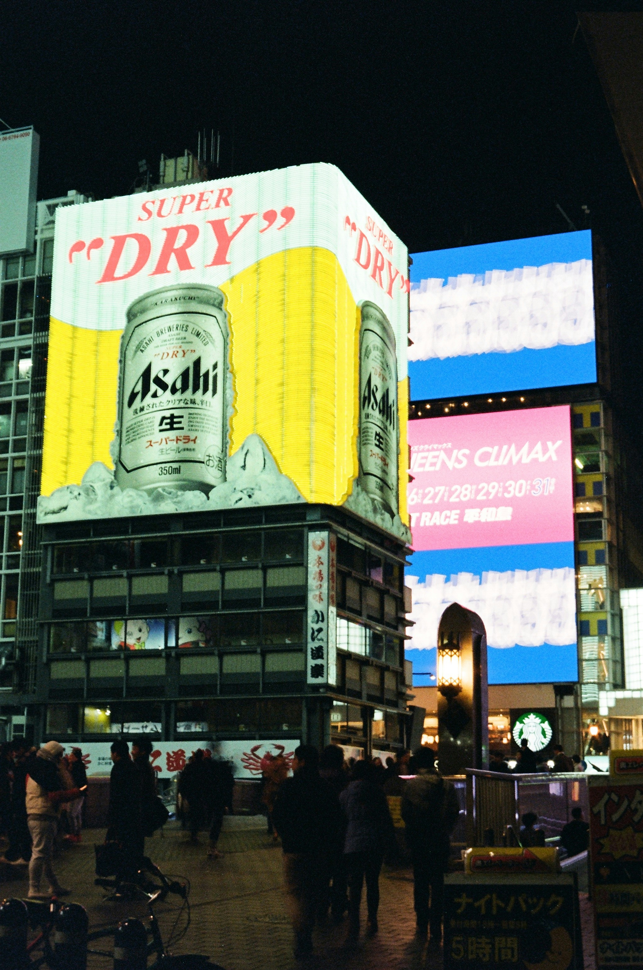 Bright billboards illuminate a busy city street at night.