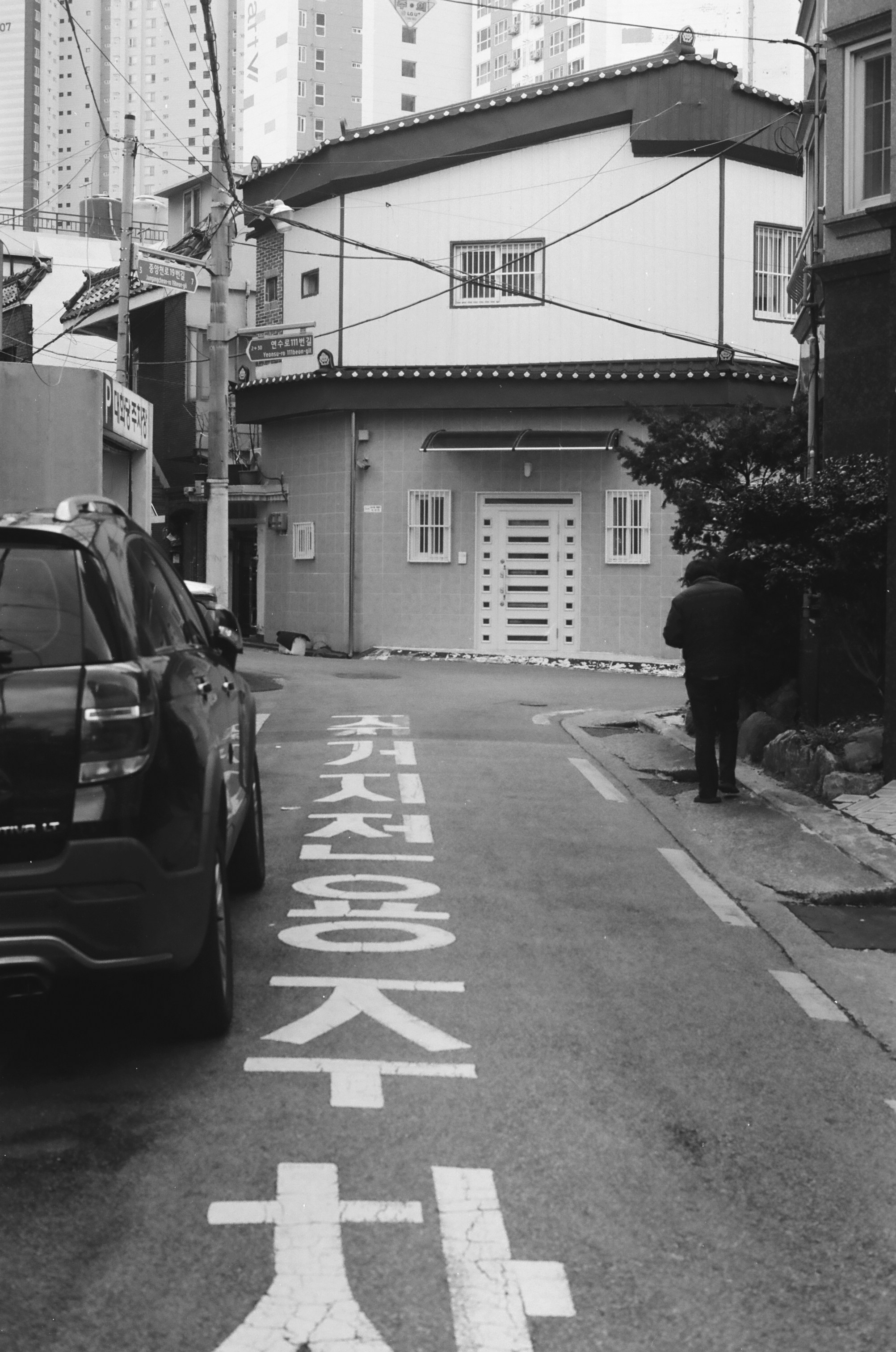 A person walks down a narrow street with cars.