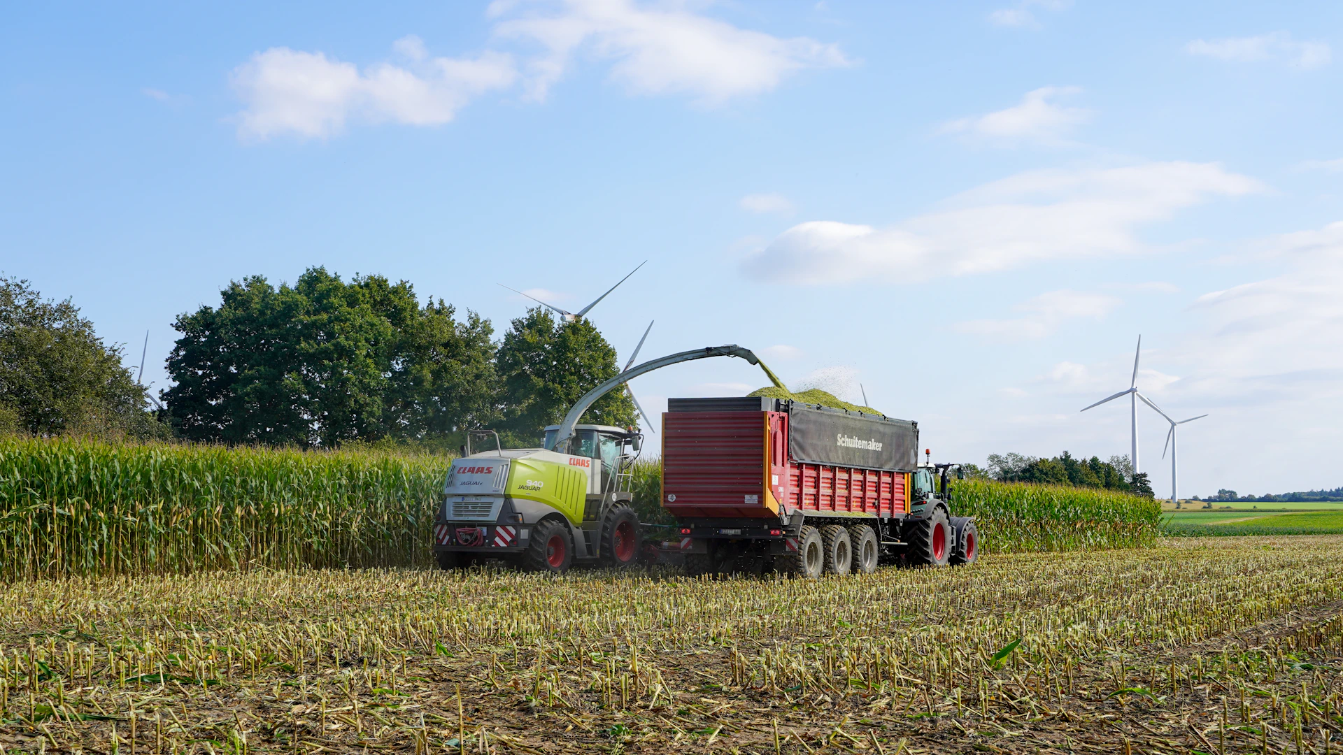 Tractor harvesting corn into a trailer in a field.