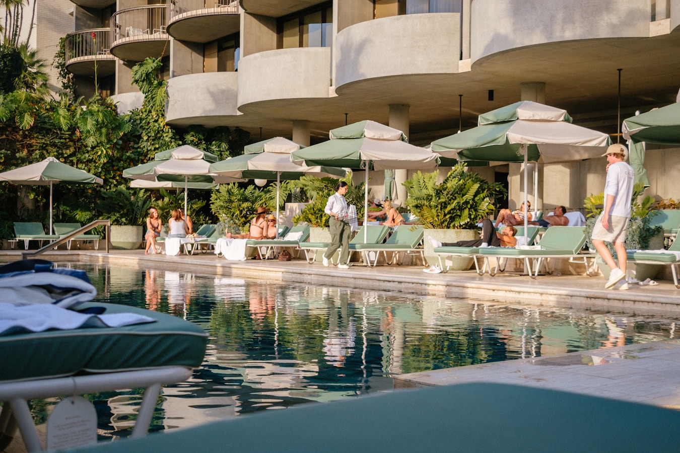 People relaxing by a resort swimming pool with lounge chairs.