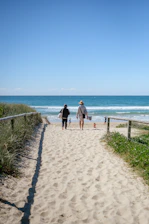 Two people walk down a sandy path to the ocean.