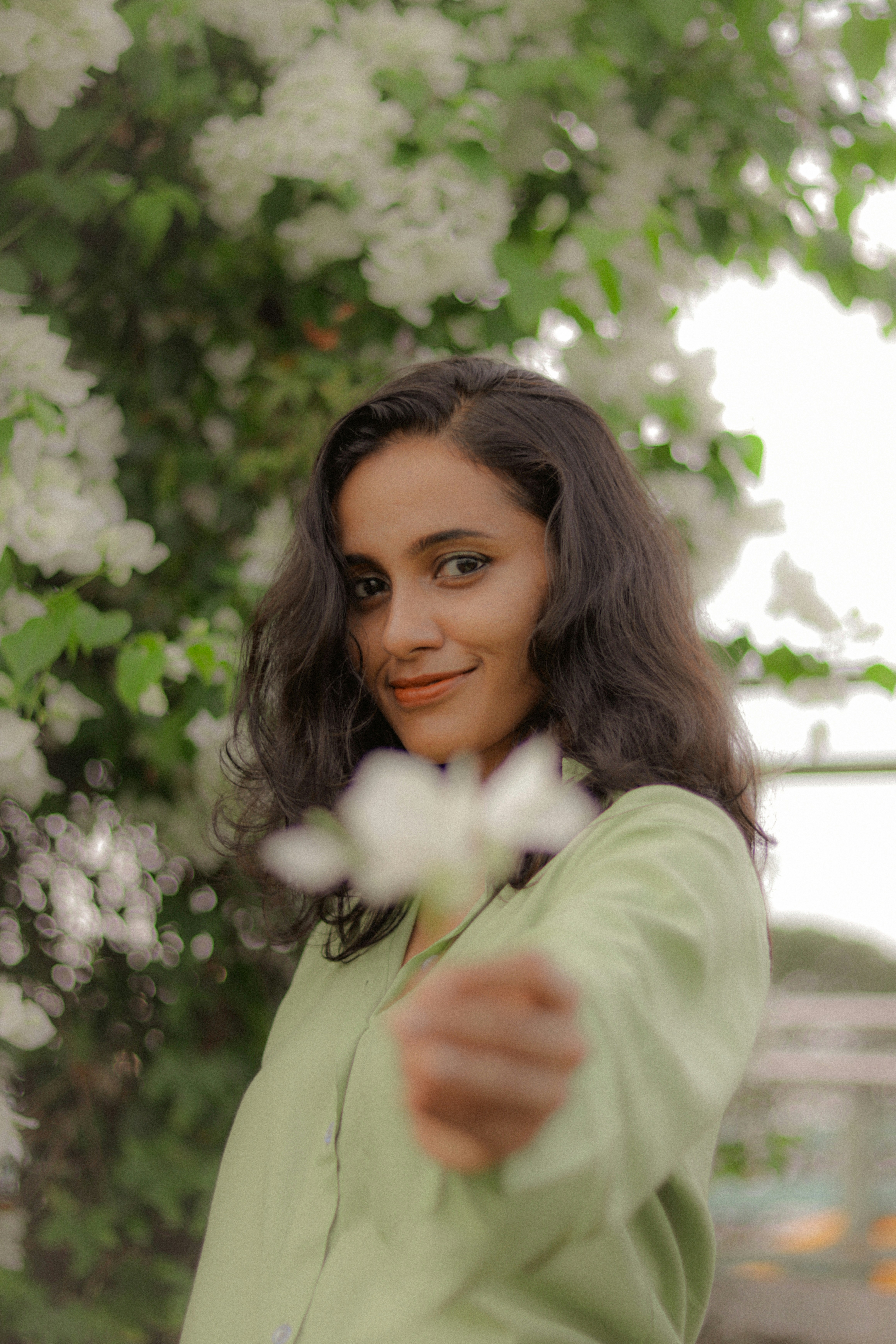 Young woman holding a white flower in front of greenery