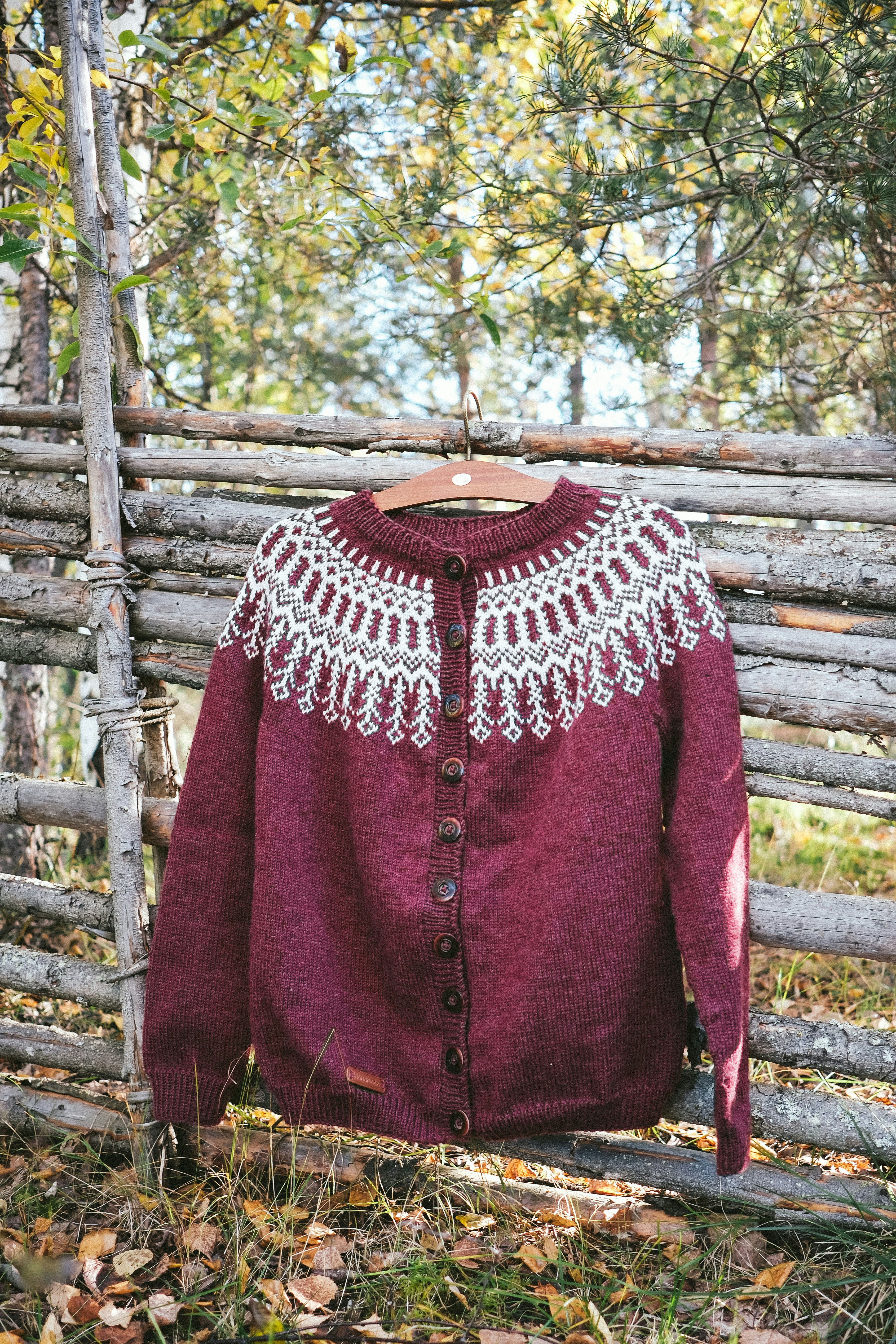 Maroon knitted sweater with folk pattern hanging outdoors.