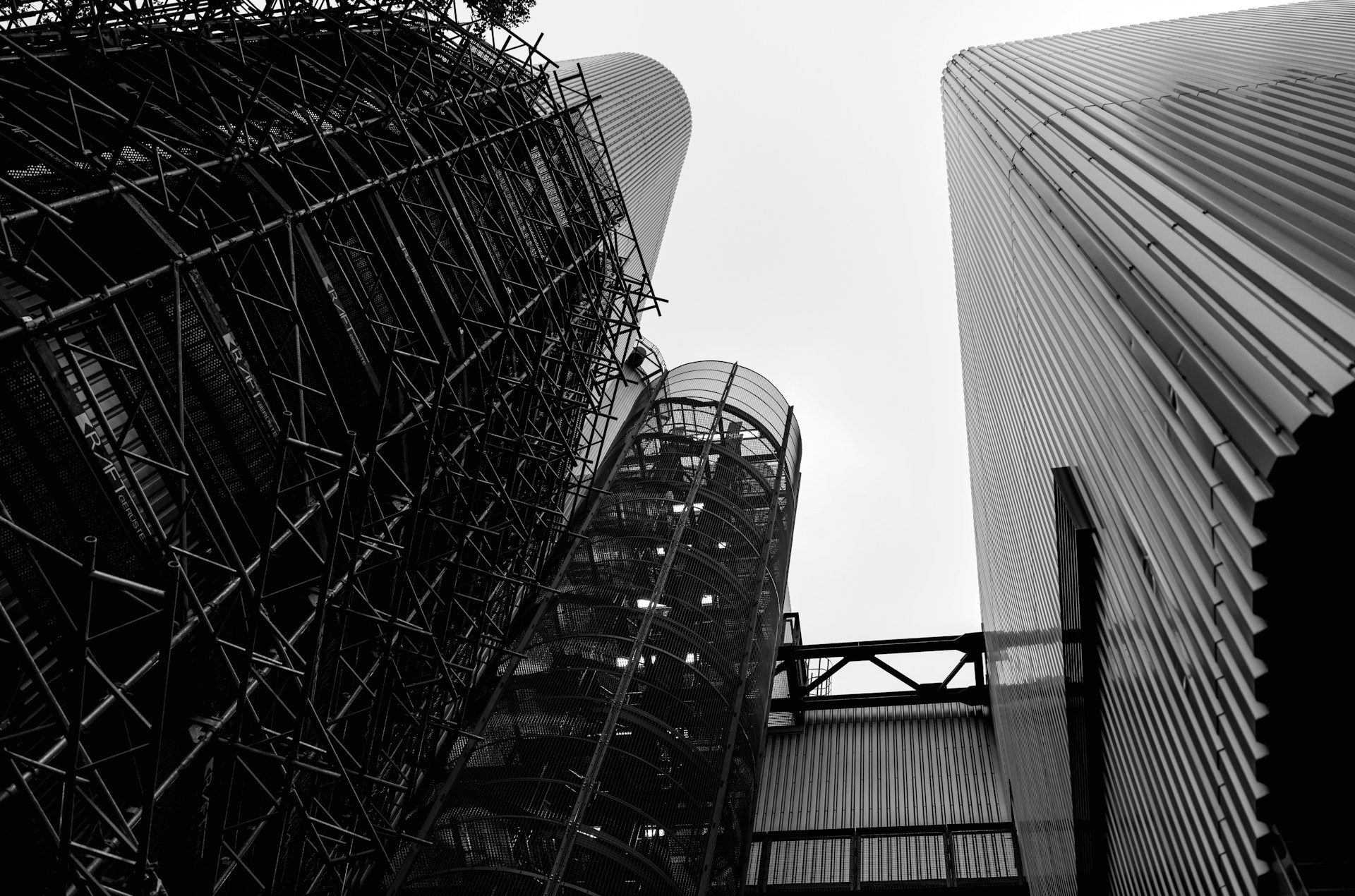 Industrial structures with scaffolding against a cloudy sky.