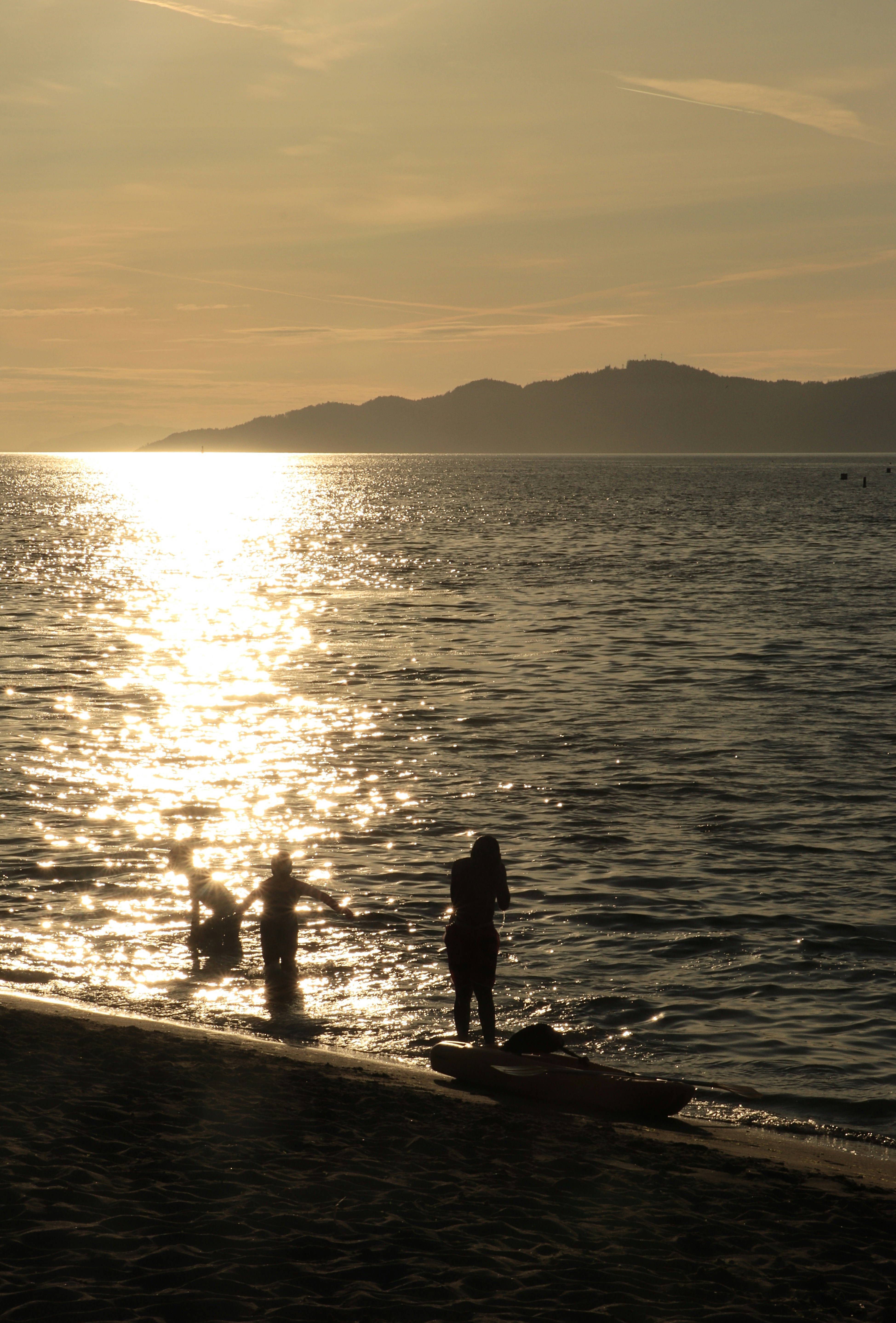 Silhouettes of people in the water near a kayak on a sandy beach