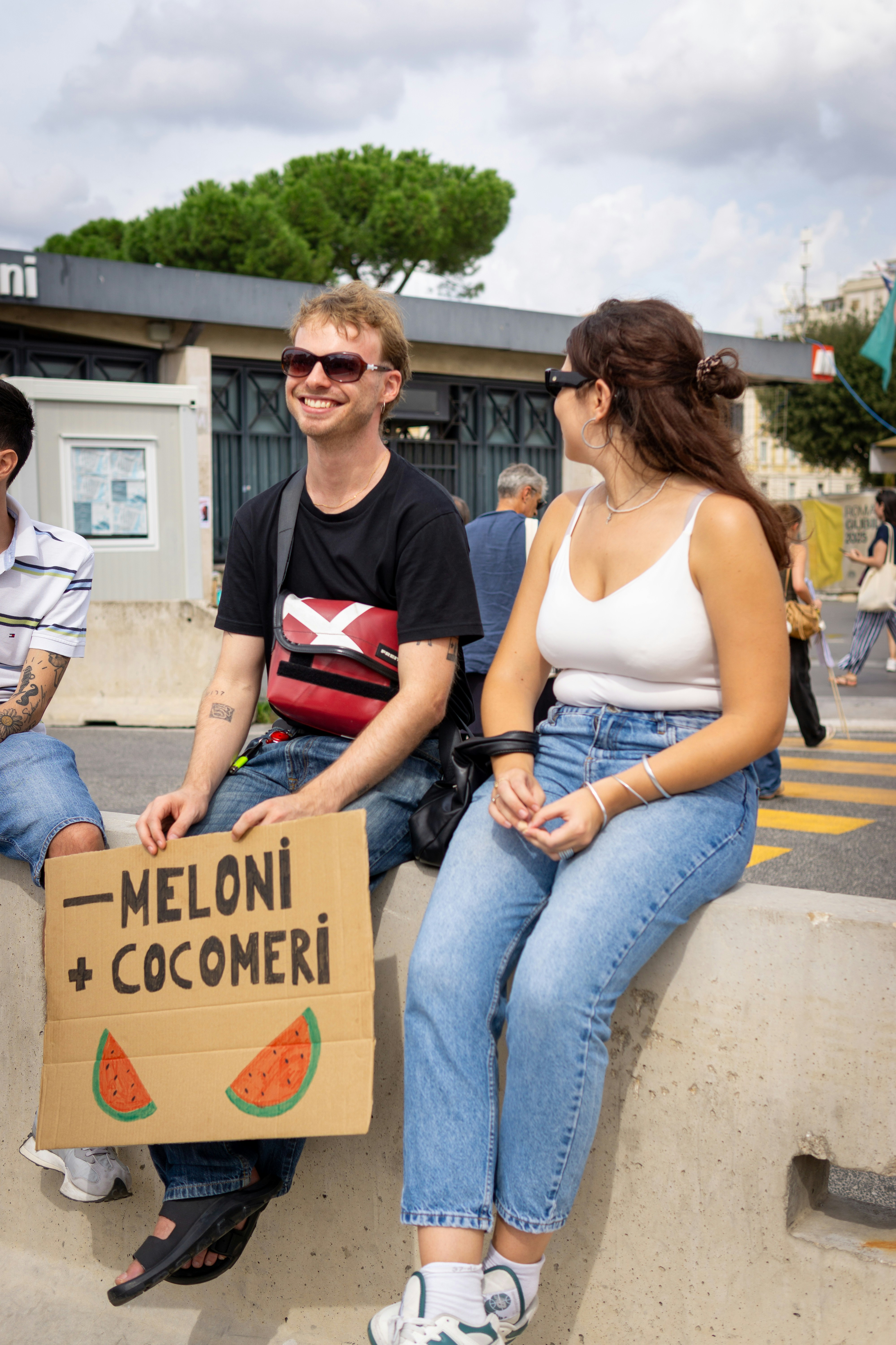 Two people sitting with a sign about meloni and watermelon.