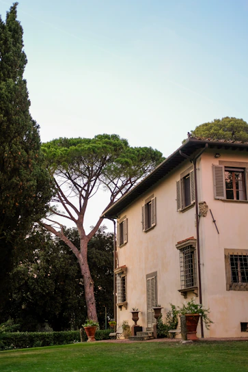 A stucco villa with tall trees and green lawn.