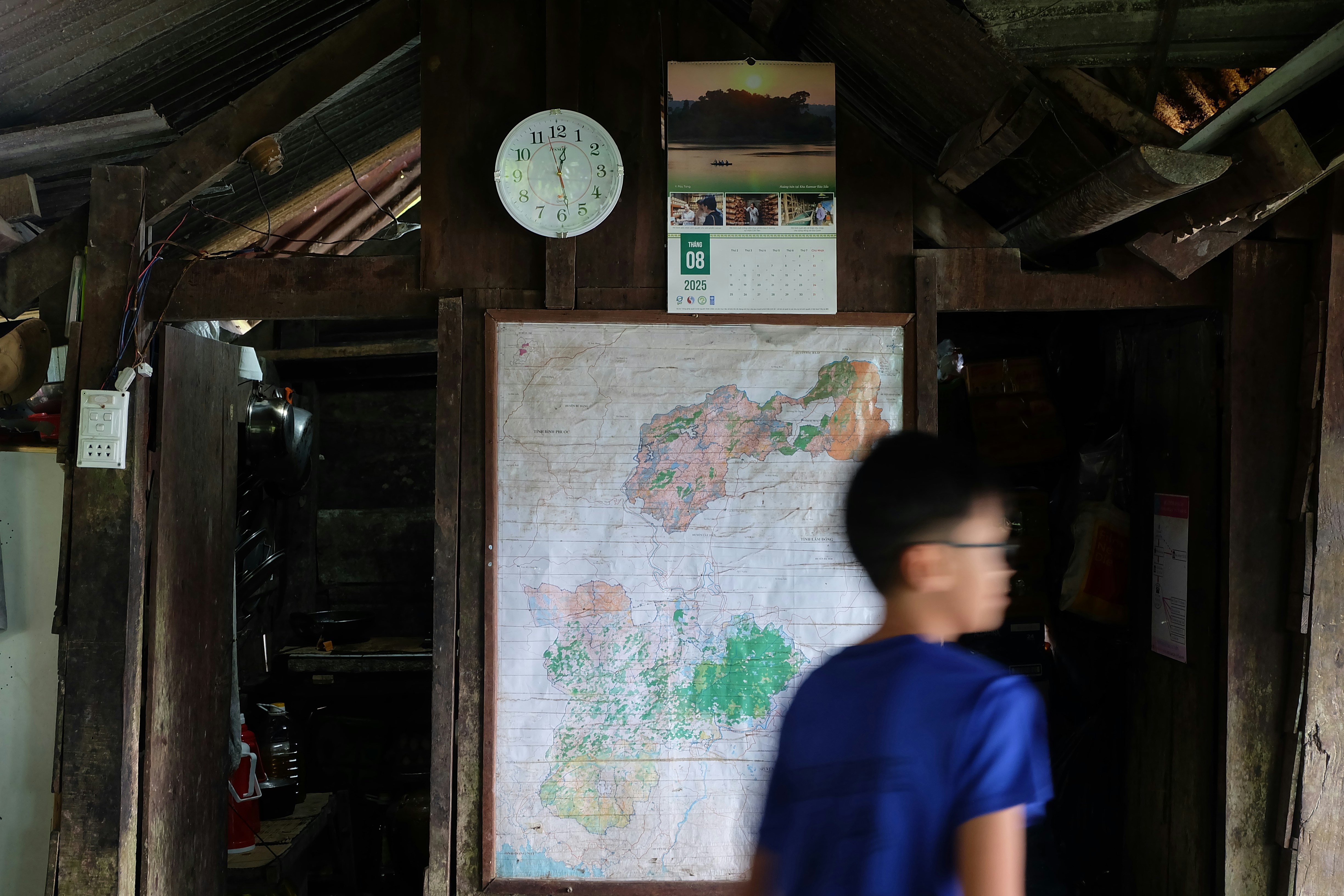 Boy walks past map and clock in rustic room.