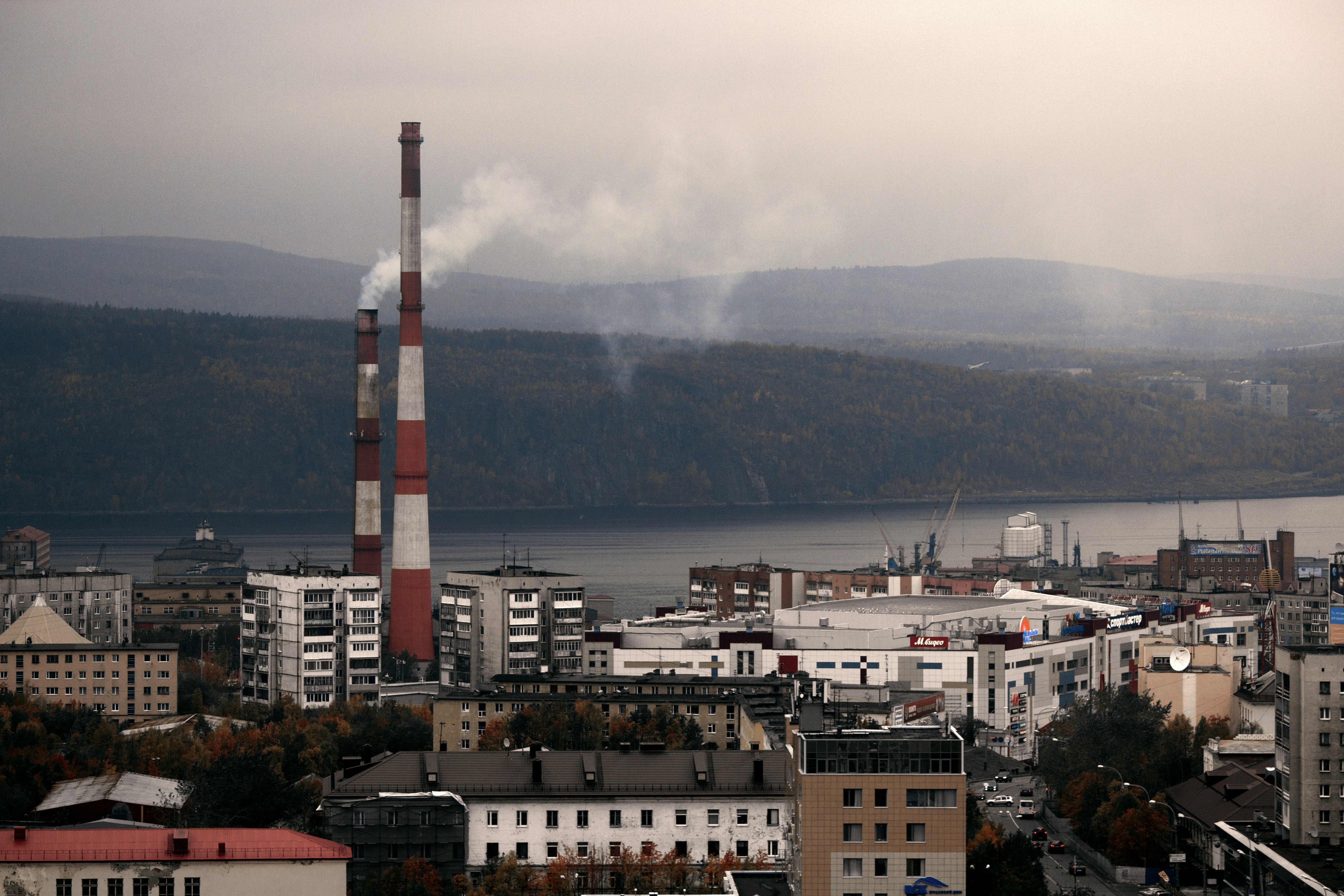 Chimeneas industriales que emiten humo sobre una ciudad junto al agua.