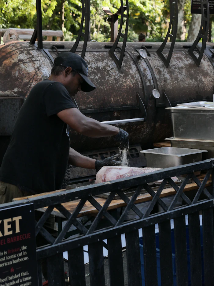 A cook in gloves working at a long offset smoker