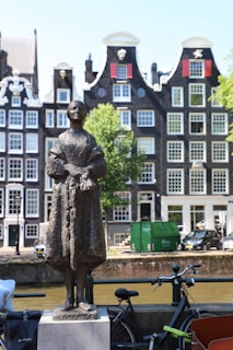 Bronze statue stands before historic amsterdam canal houses