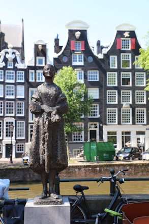 Bronze statue stands before historic amsterdam canal houses