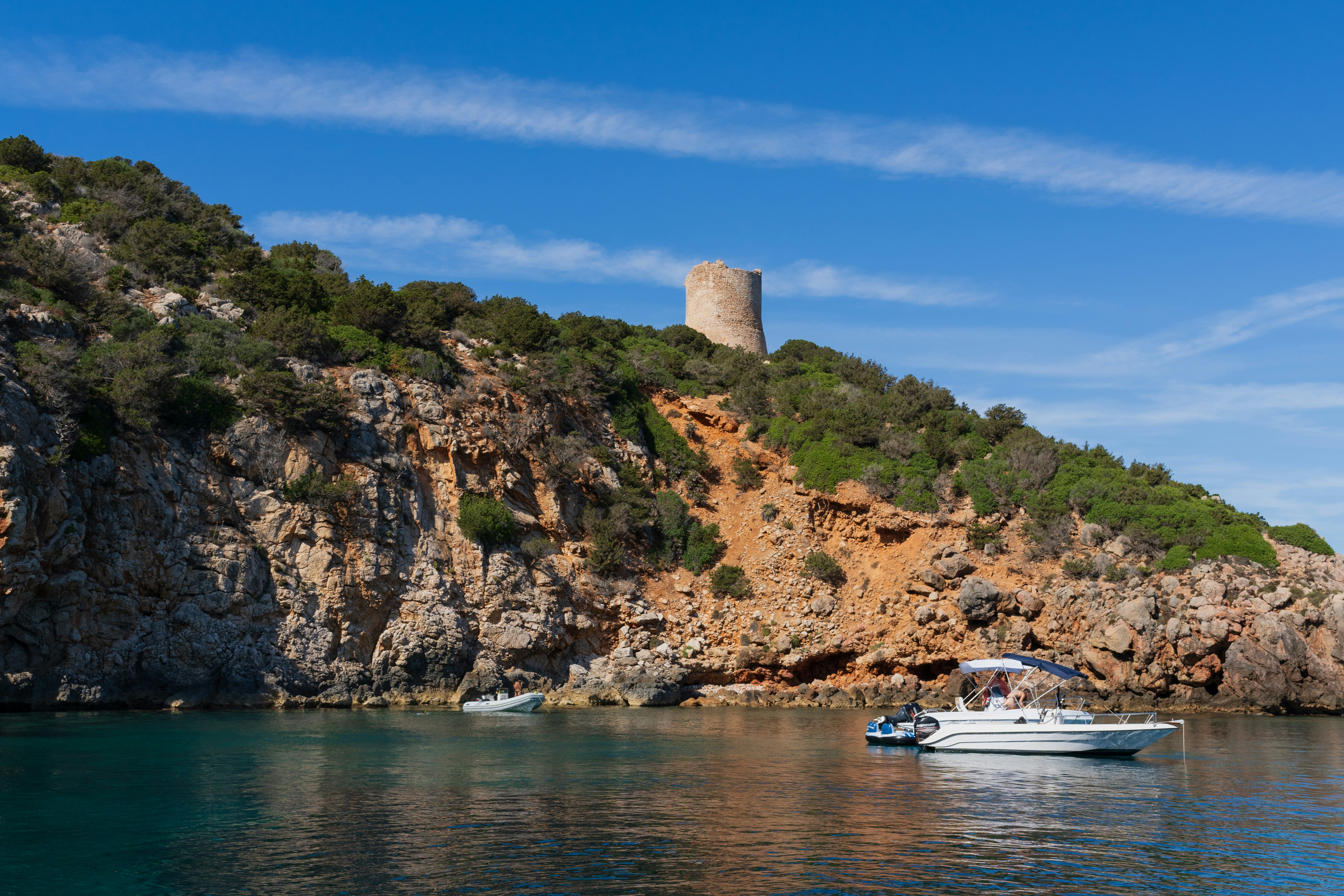 Torre de pedra em uma ilha rochosa com barcos nas proximidades.