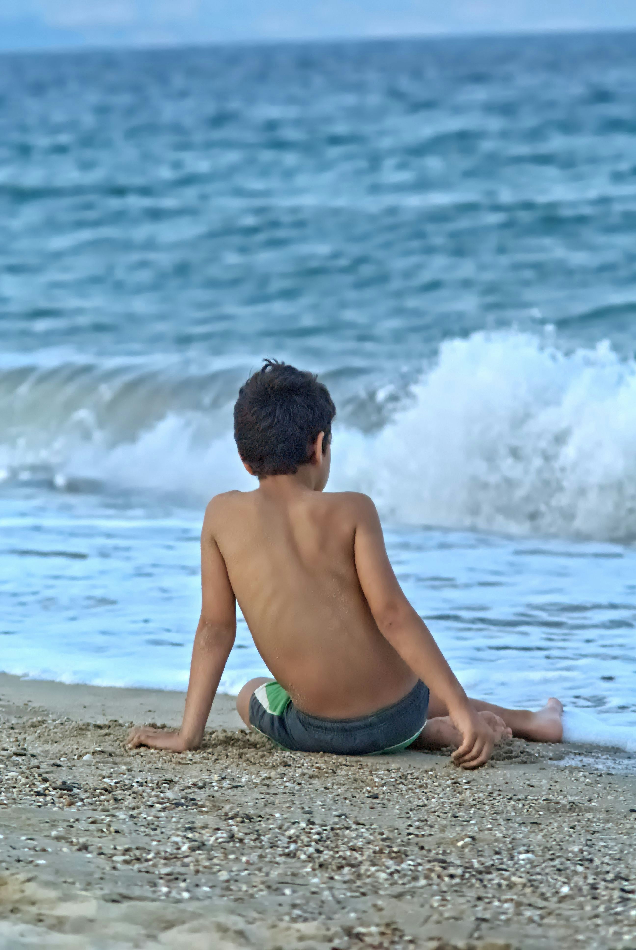 Young boy sitting on a sandy beach watching waves