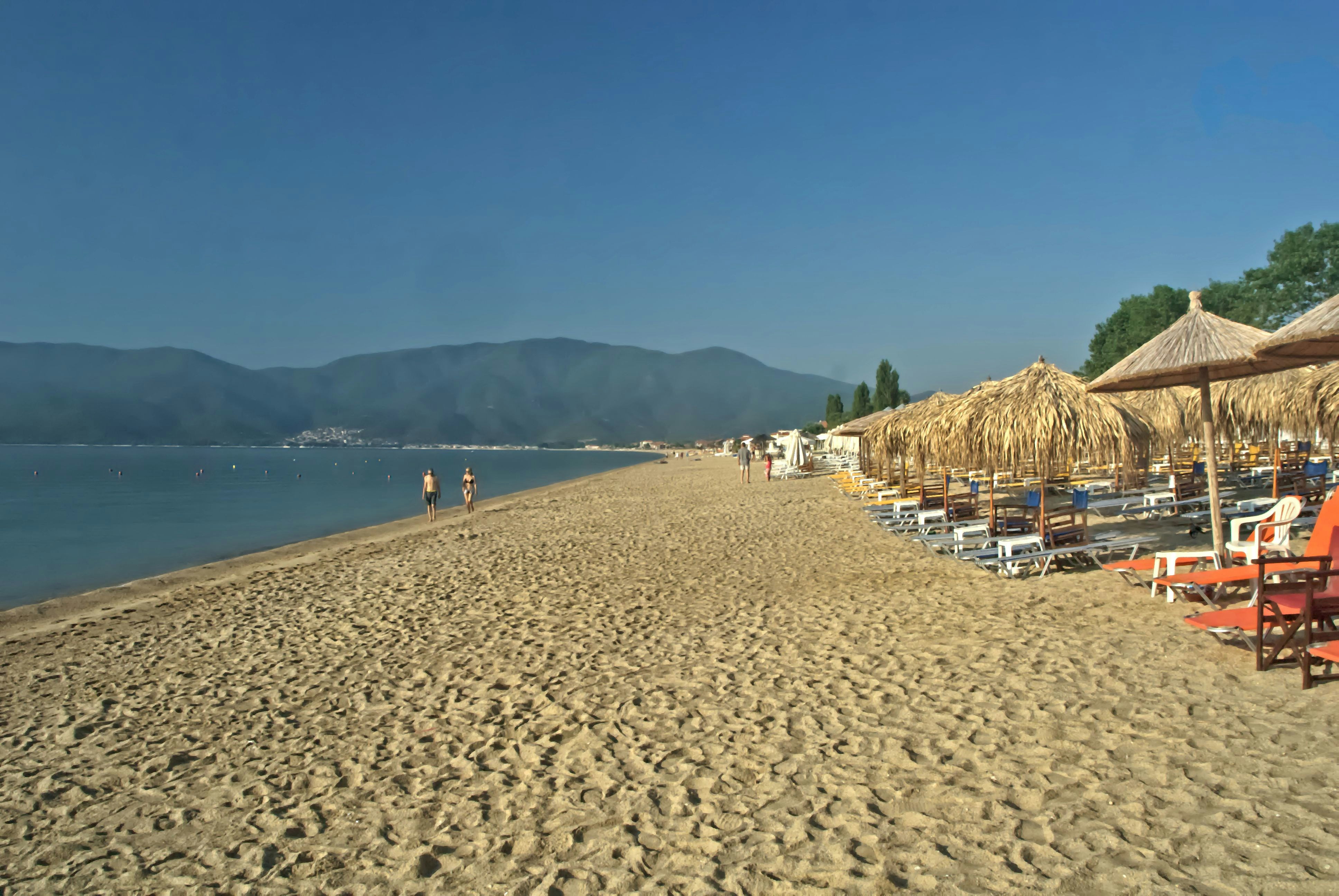 Sandy beach with straw umbrellas and lounge chairs.