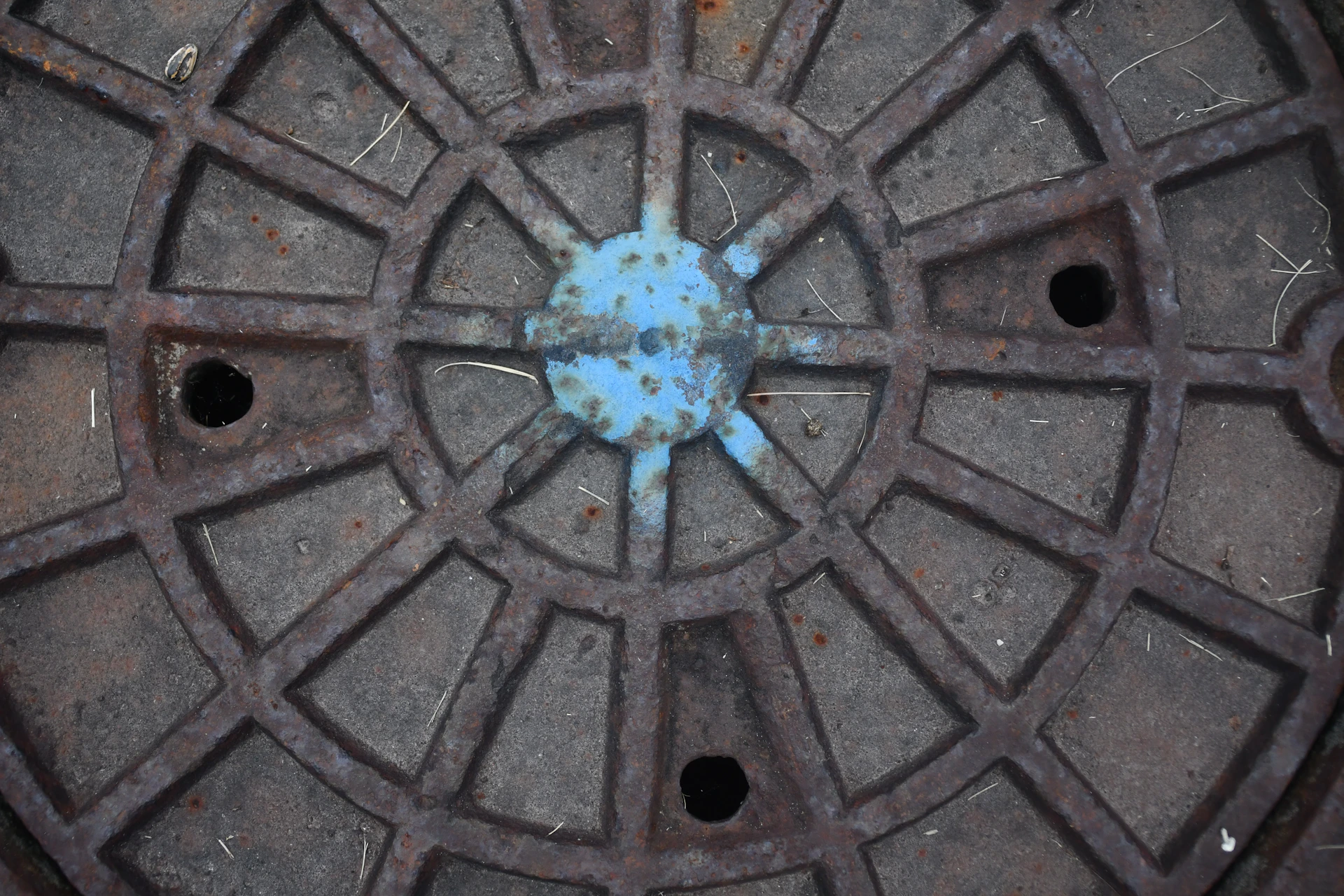 Close-up of a rusty manhole cover with blue paint