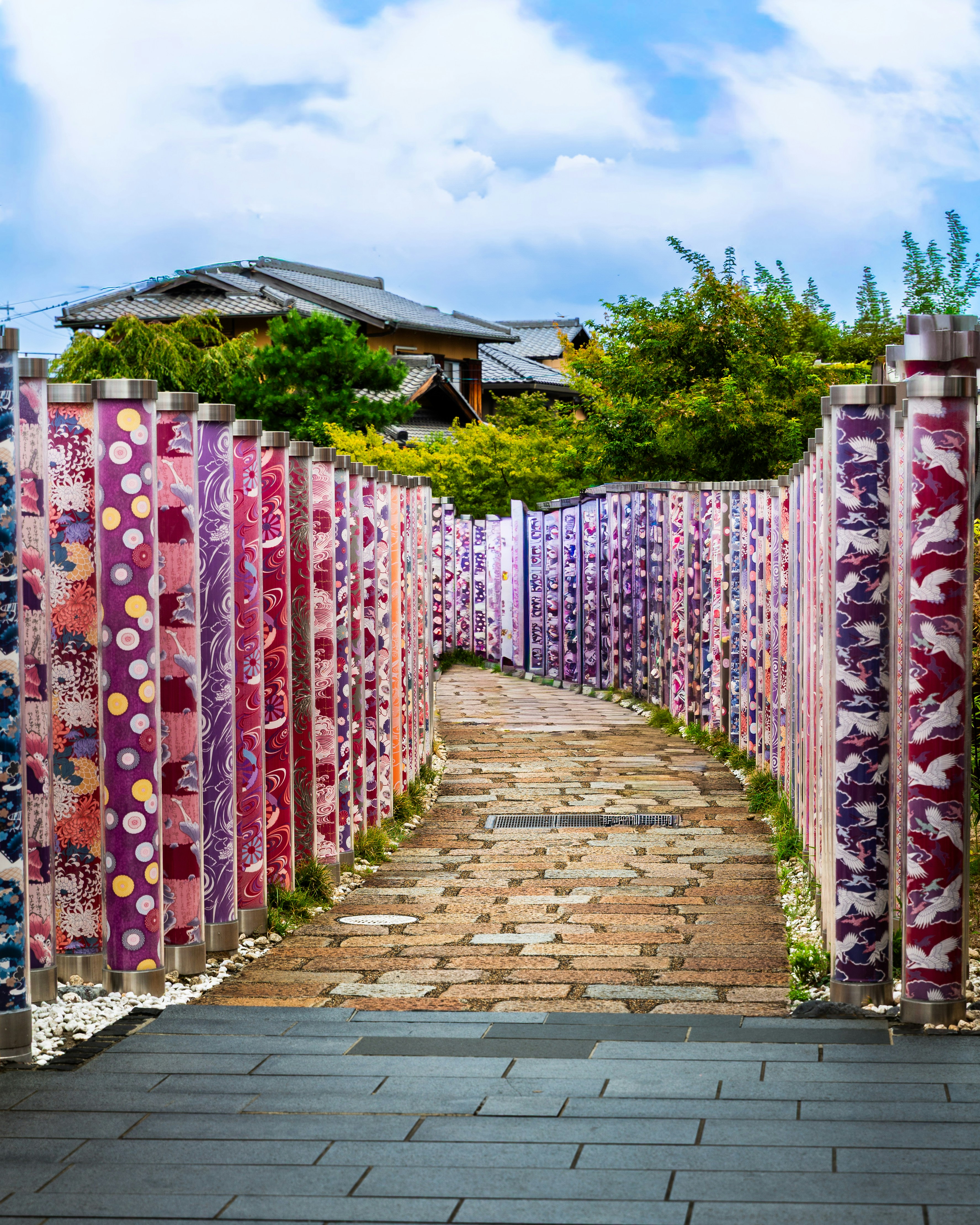 Colorful patterned pillars line a brick pathway through greenery.