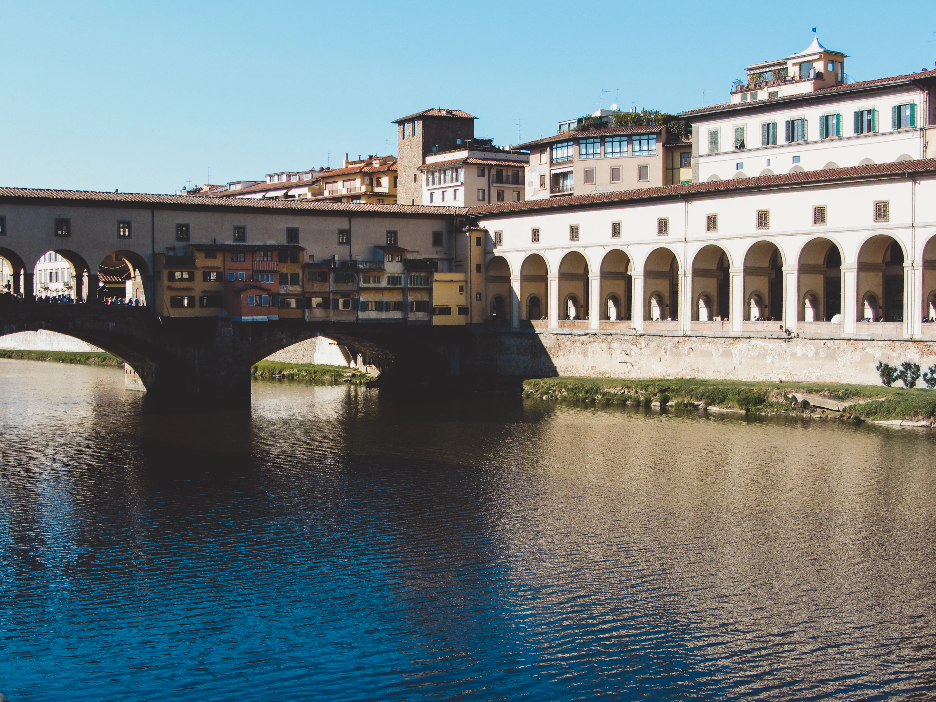 The Ponte Vecchio spanning the Arno, its ochre shops jutting out over the water beside a long arcaded riverside gallery