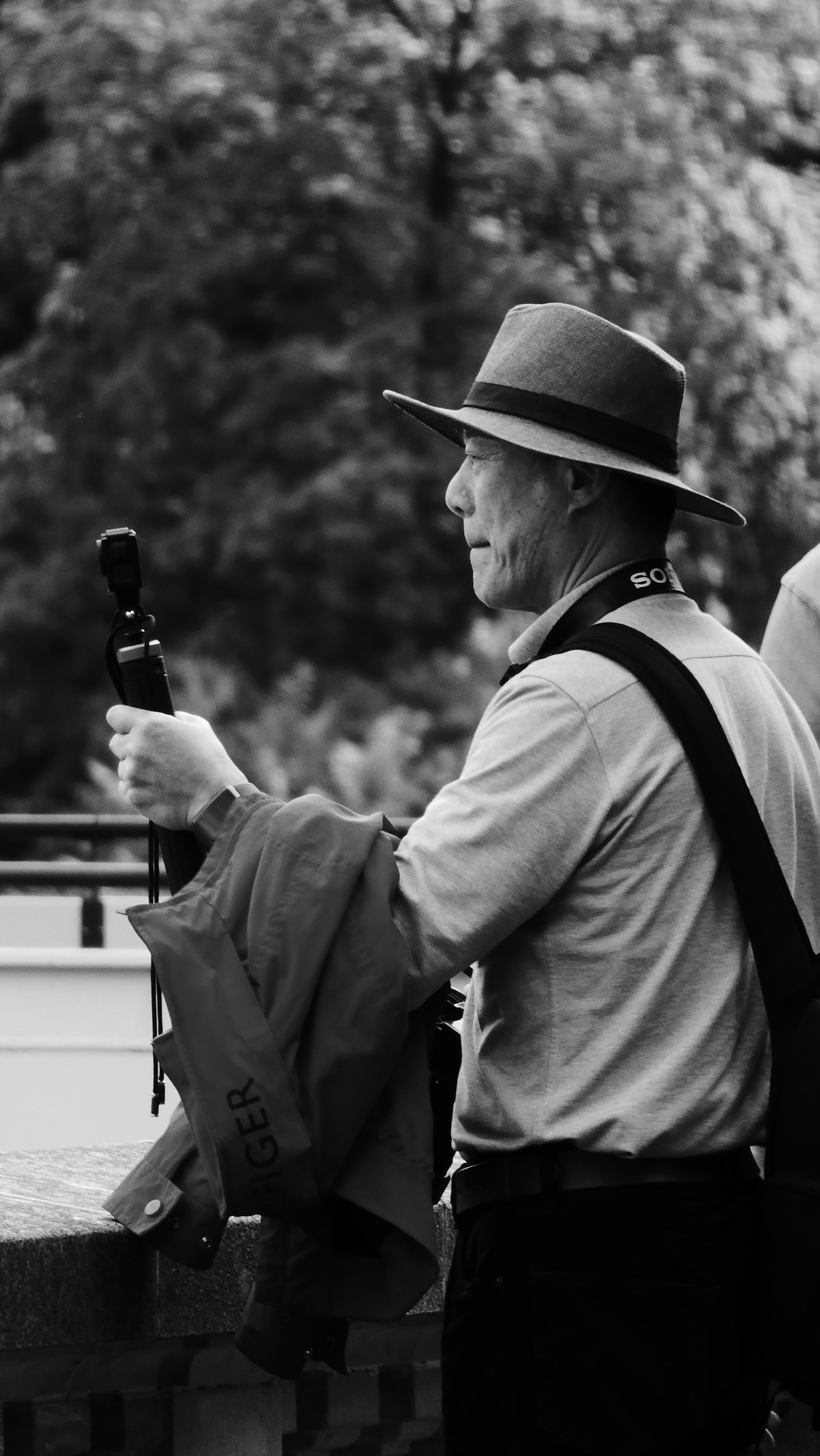 Man in hat holds camera, with jacket draped over arm.