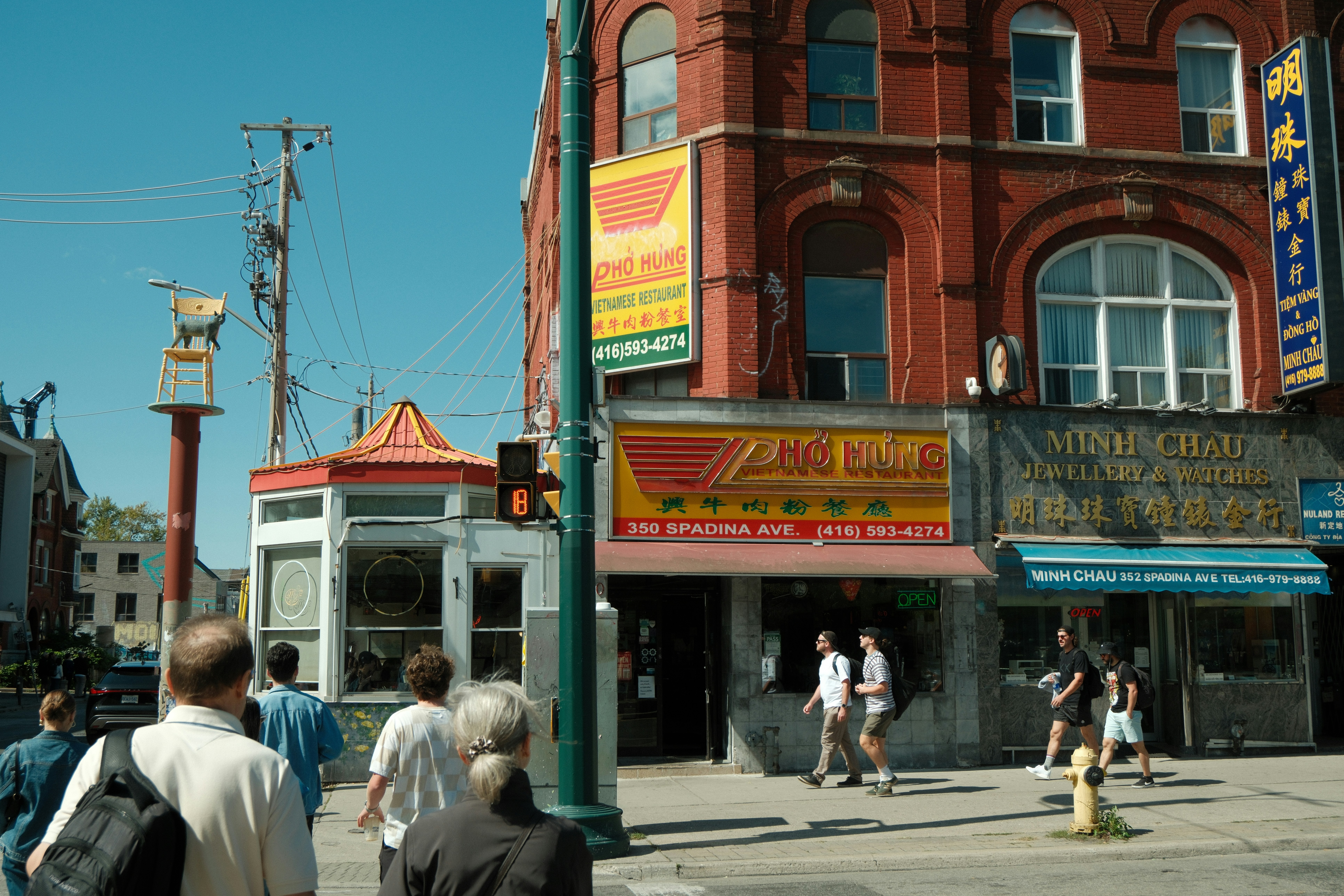 People walk past shops on a sunny city street.