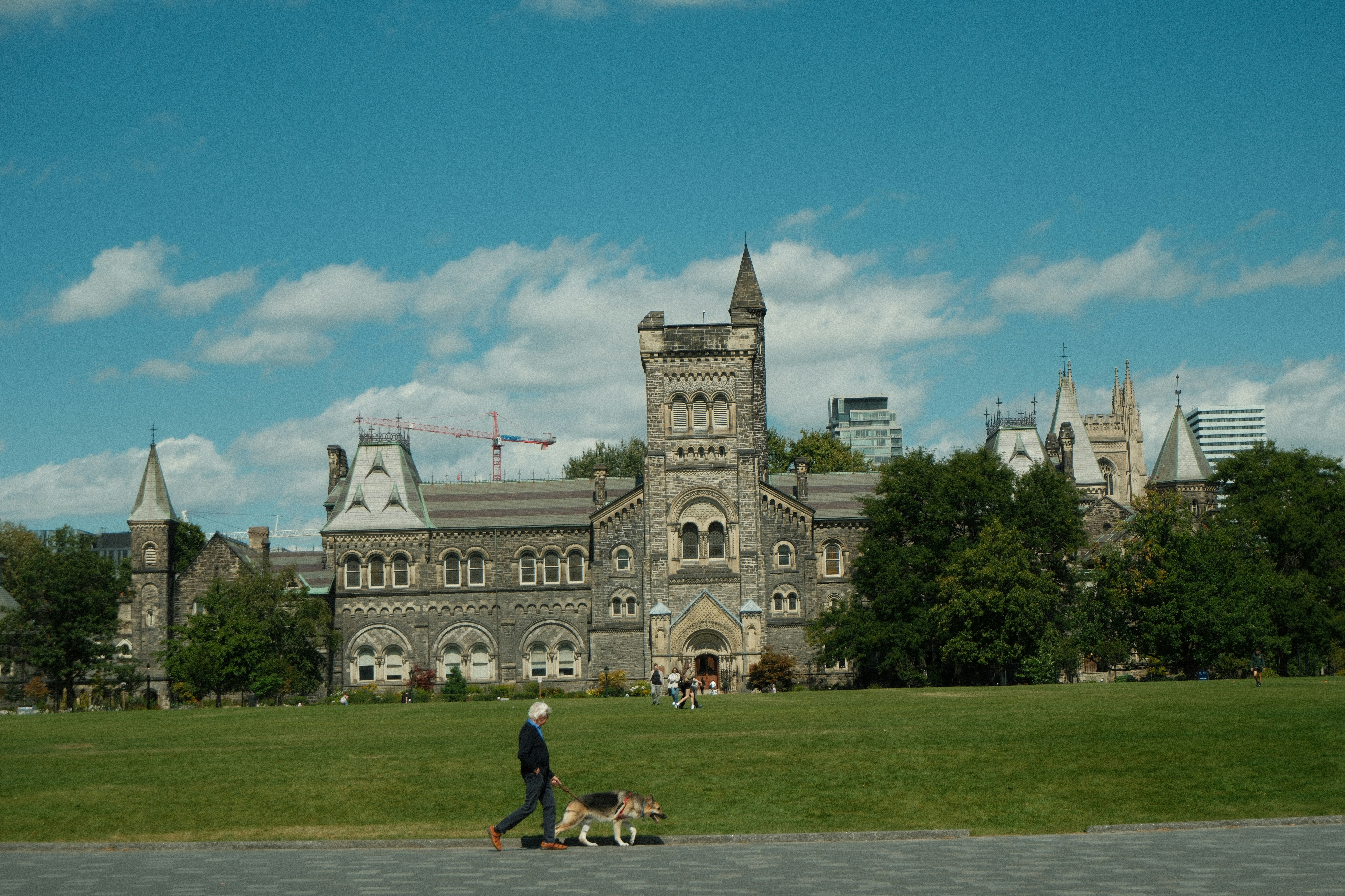 Person walks dog on grassy field near university building
