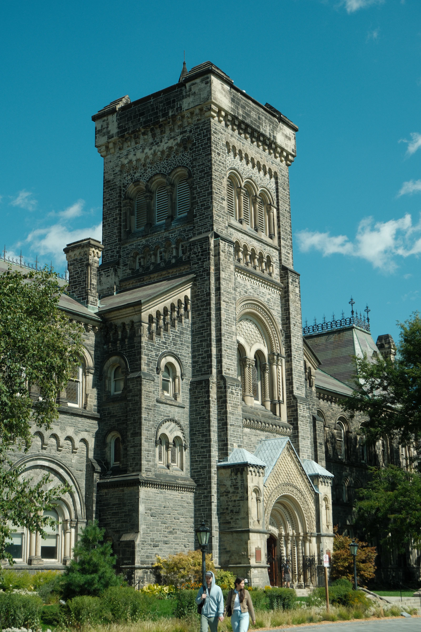 A stone university building with a tall tower, surrounded by trees