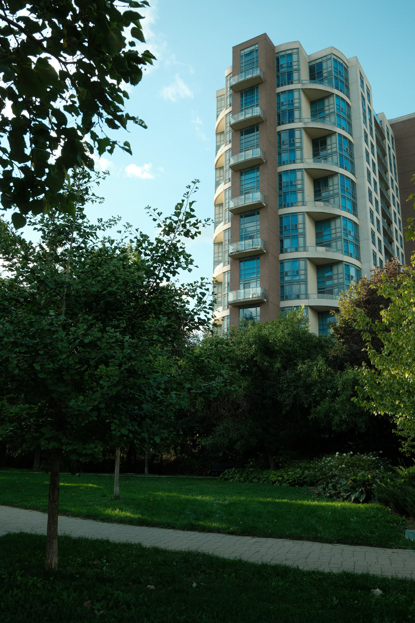 A modern apartment building with rows of balconies framed by green trees in an Ontario city