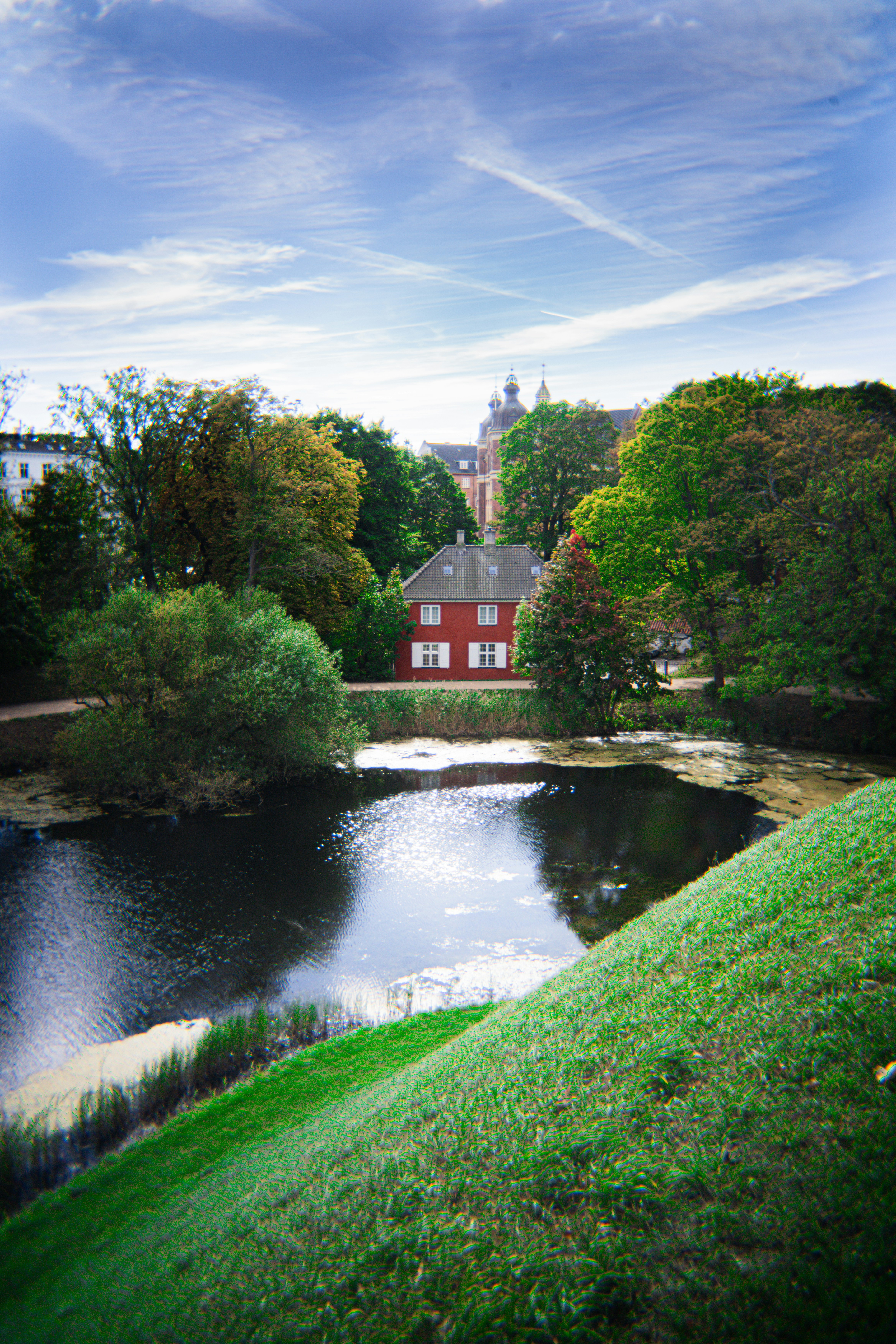 Red house beside a dark pond with trees.