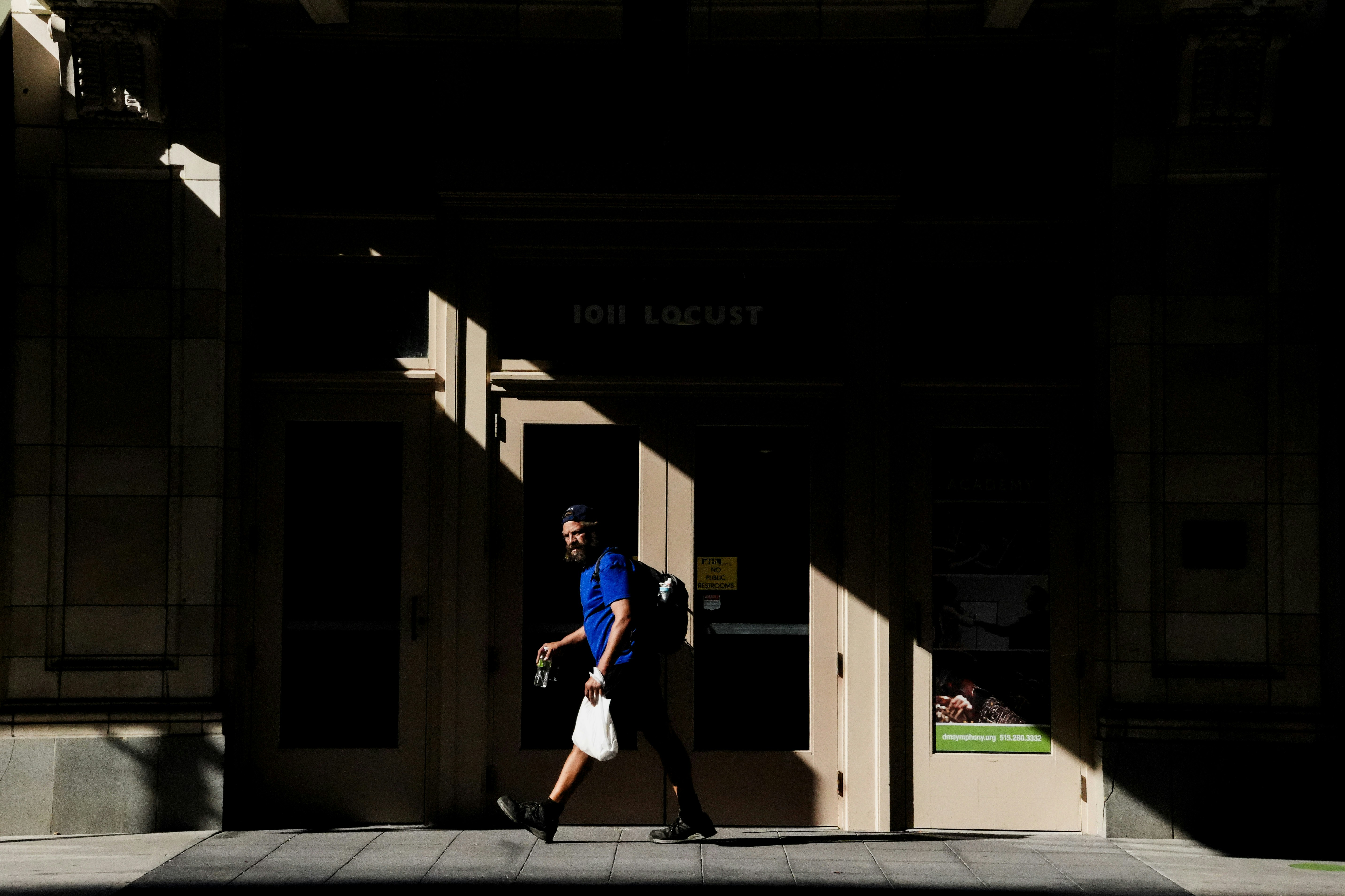 建物の外を太陽の光と影の中を歩く男。