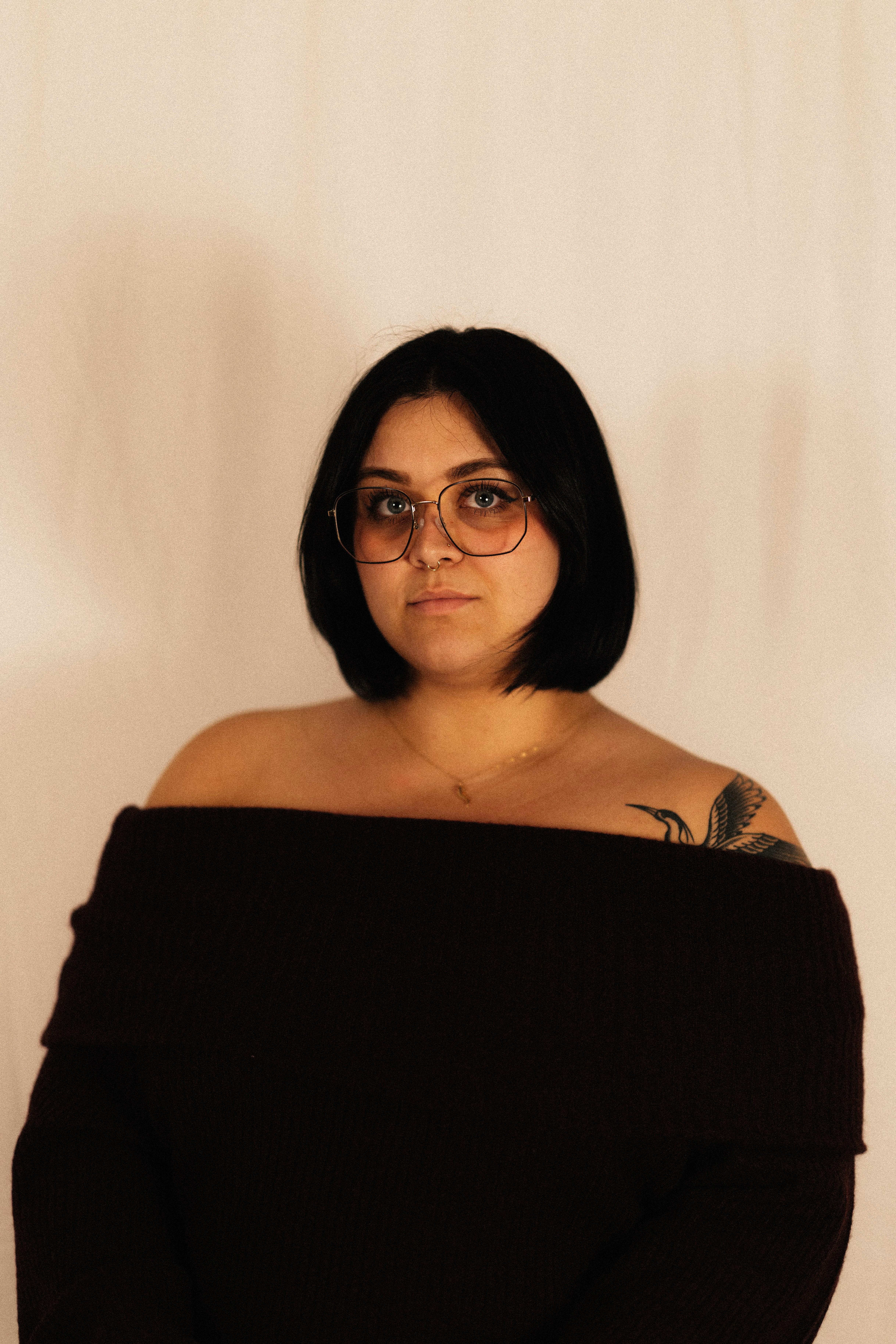 Woman with dark hair and glasses wearing off-shoulder top.