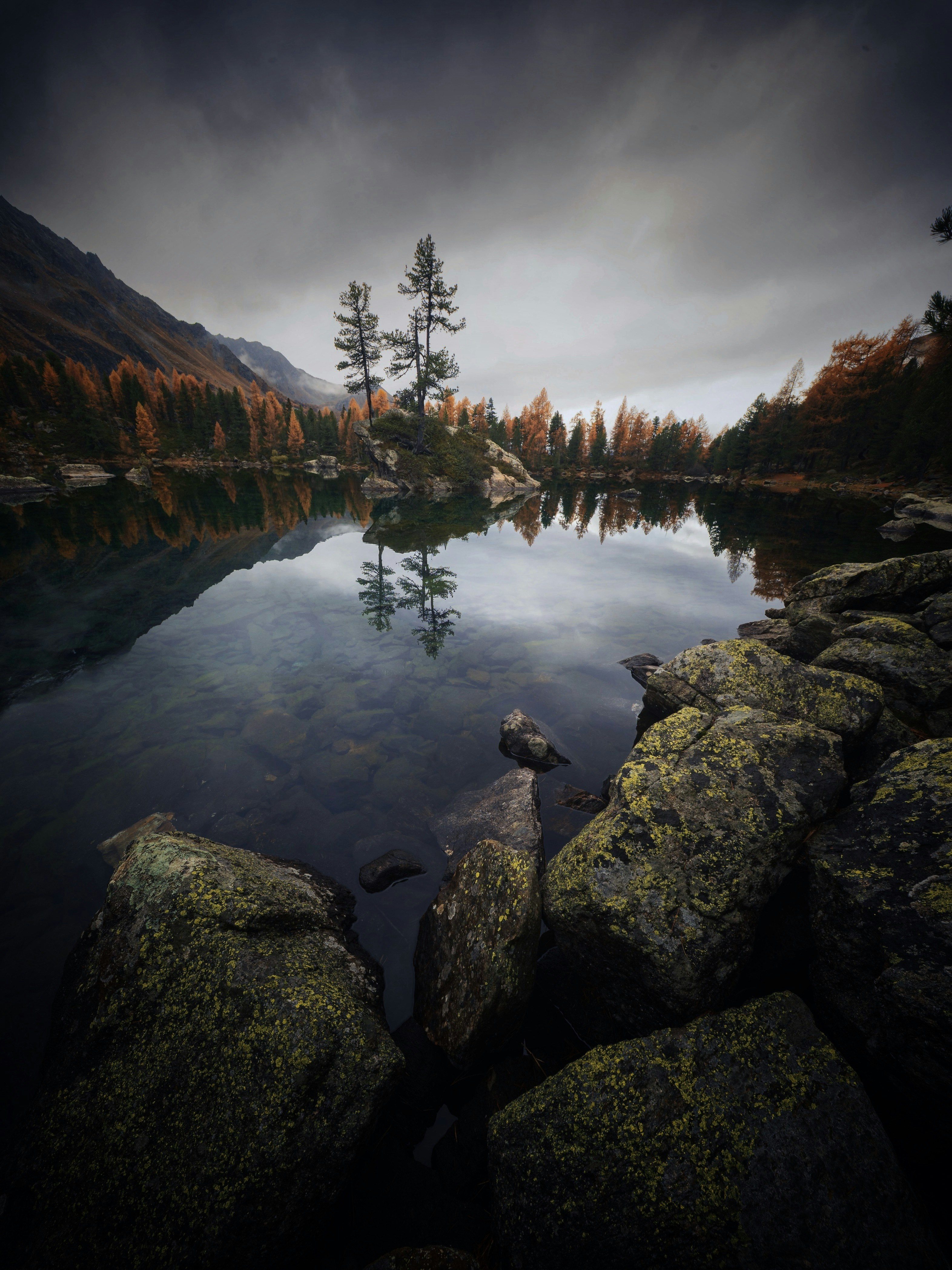 Gloomy lake with autumn trees and rocky shore.