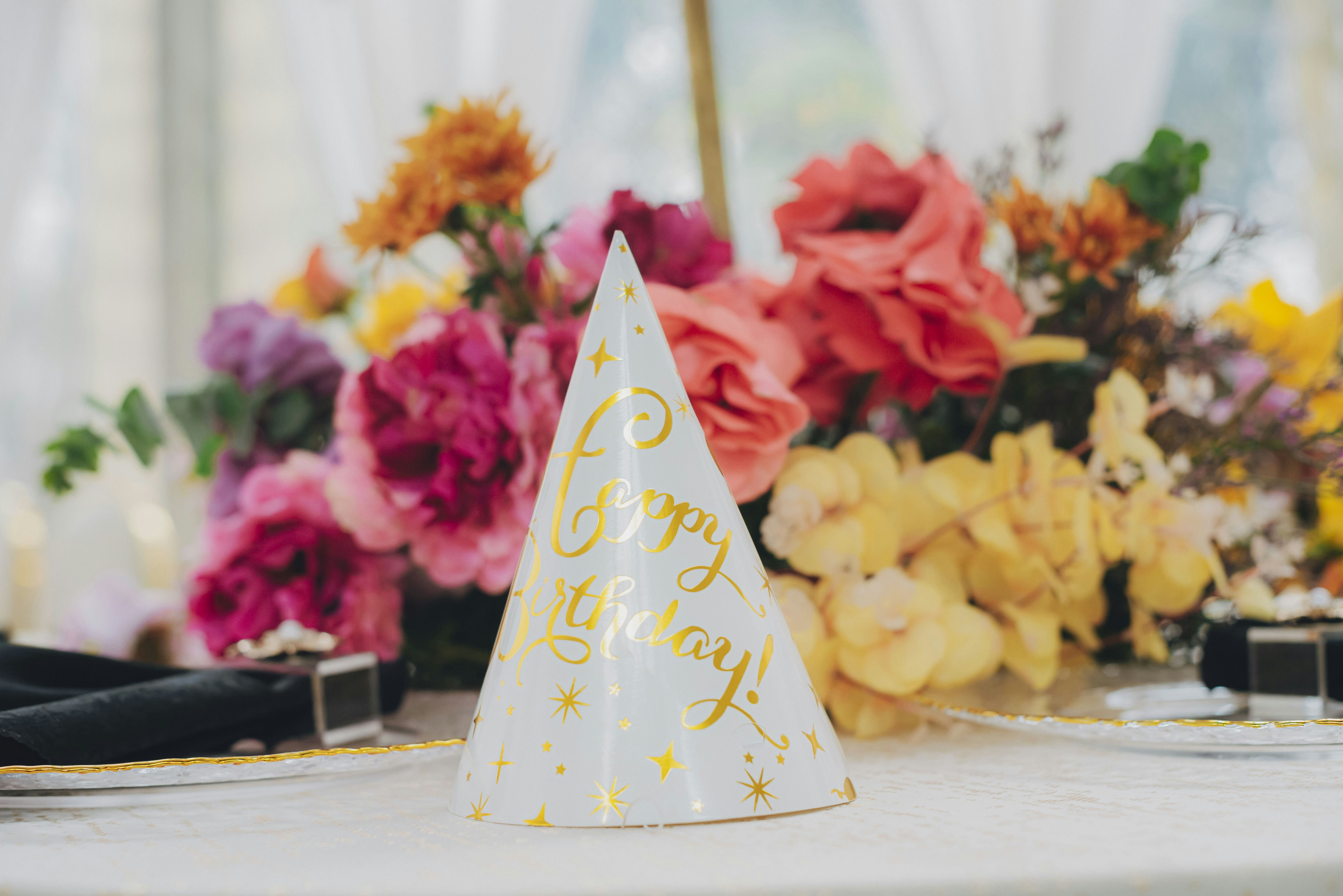 Party hat with gold stars sits before flowers.