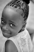 A young girl with braided hair smiles coyly.