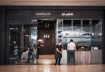 Two barbers stand at the entrance of a shop.
