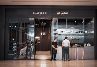 Two barbers stand at the entrance of a shop.