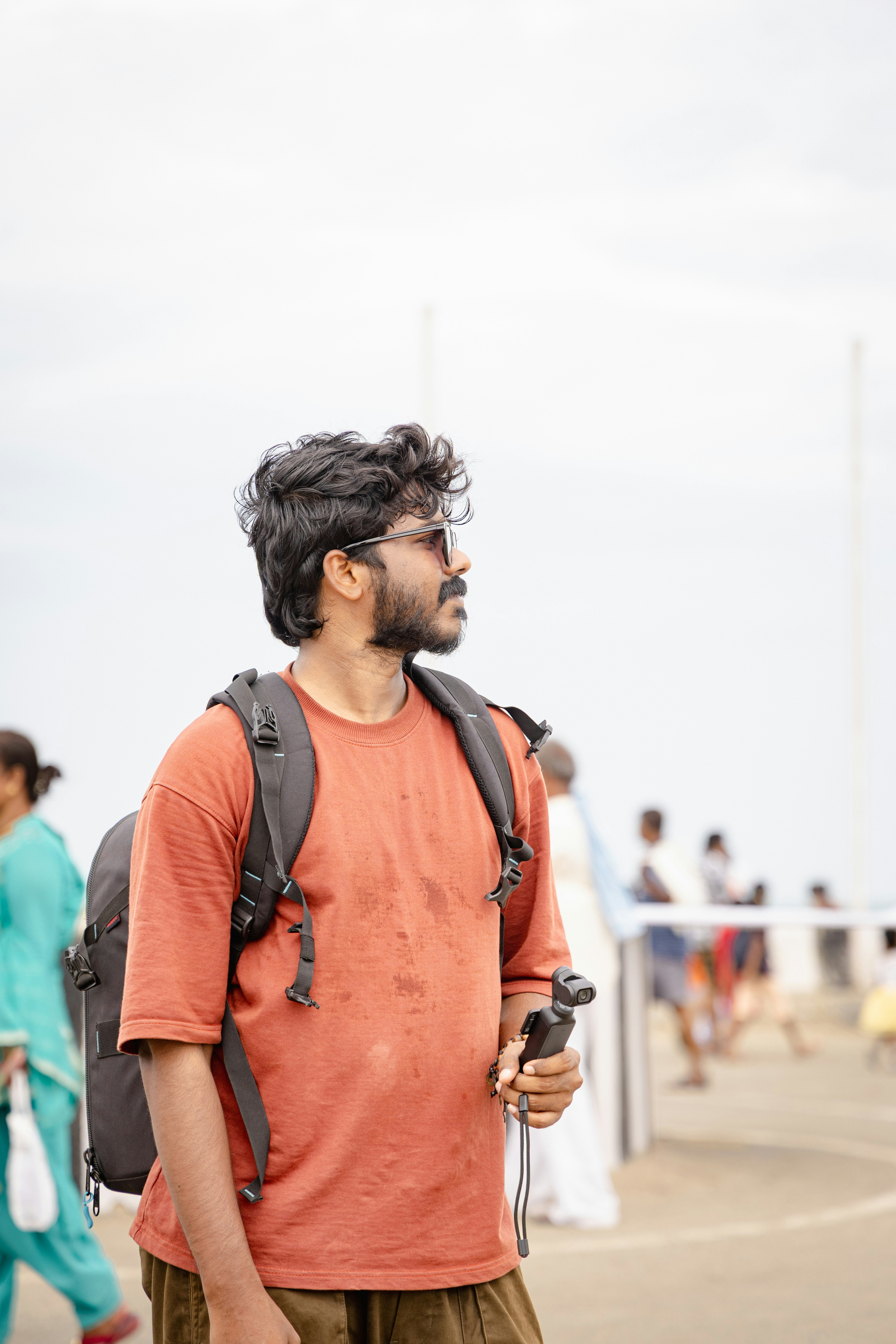 Hombre con mochila y palo de selfie mira hacia otro lado.