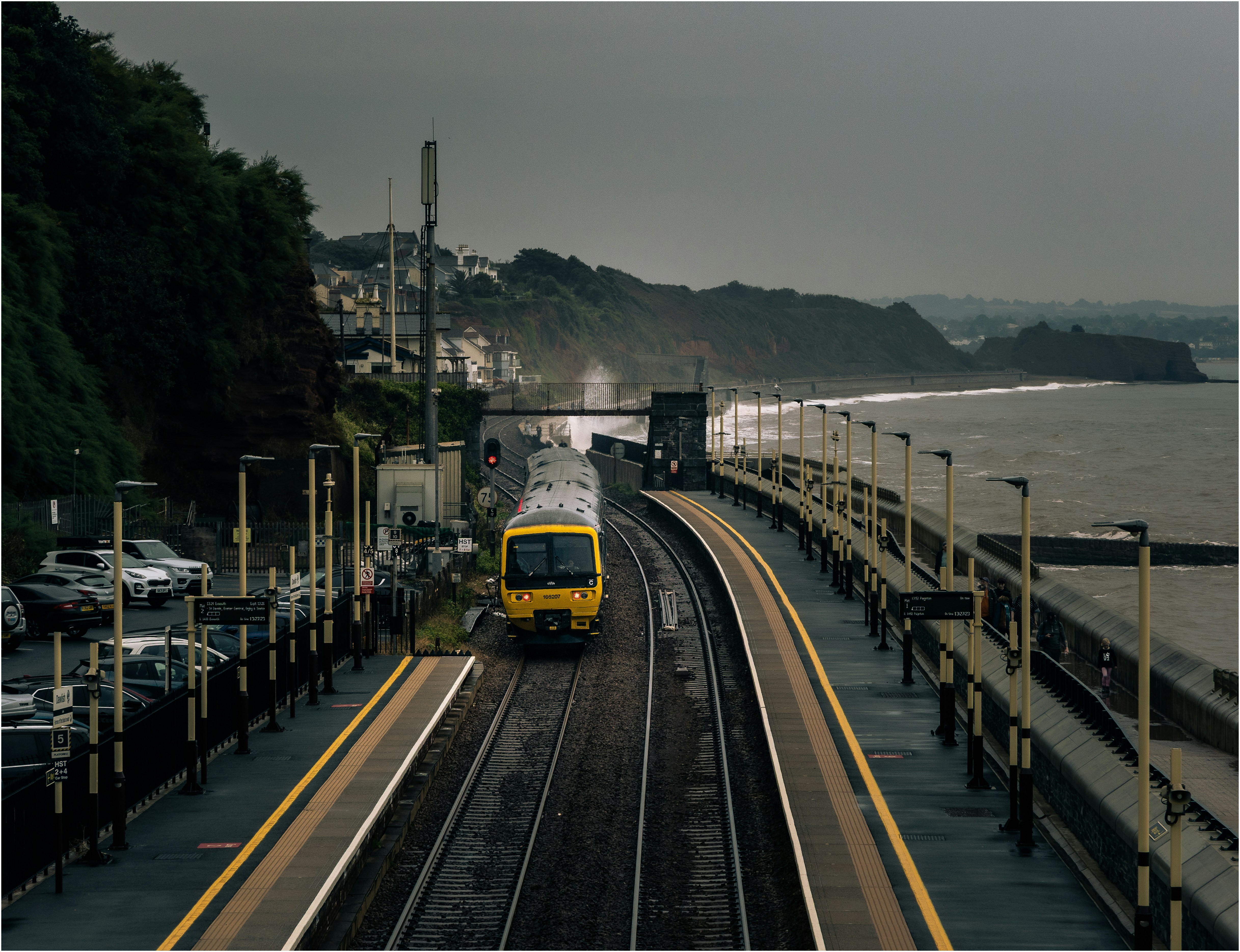A yellow train approaches a coastal station.